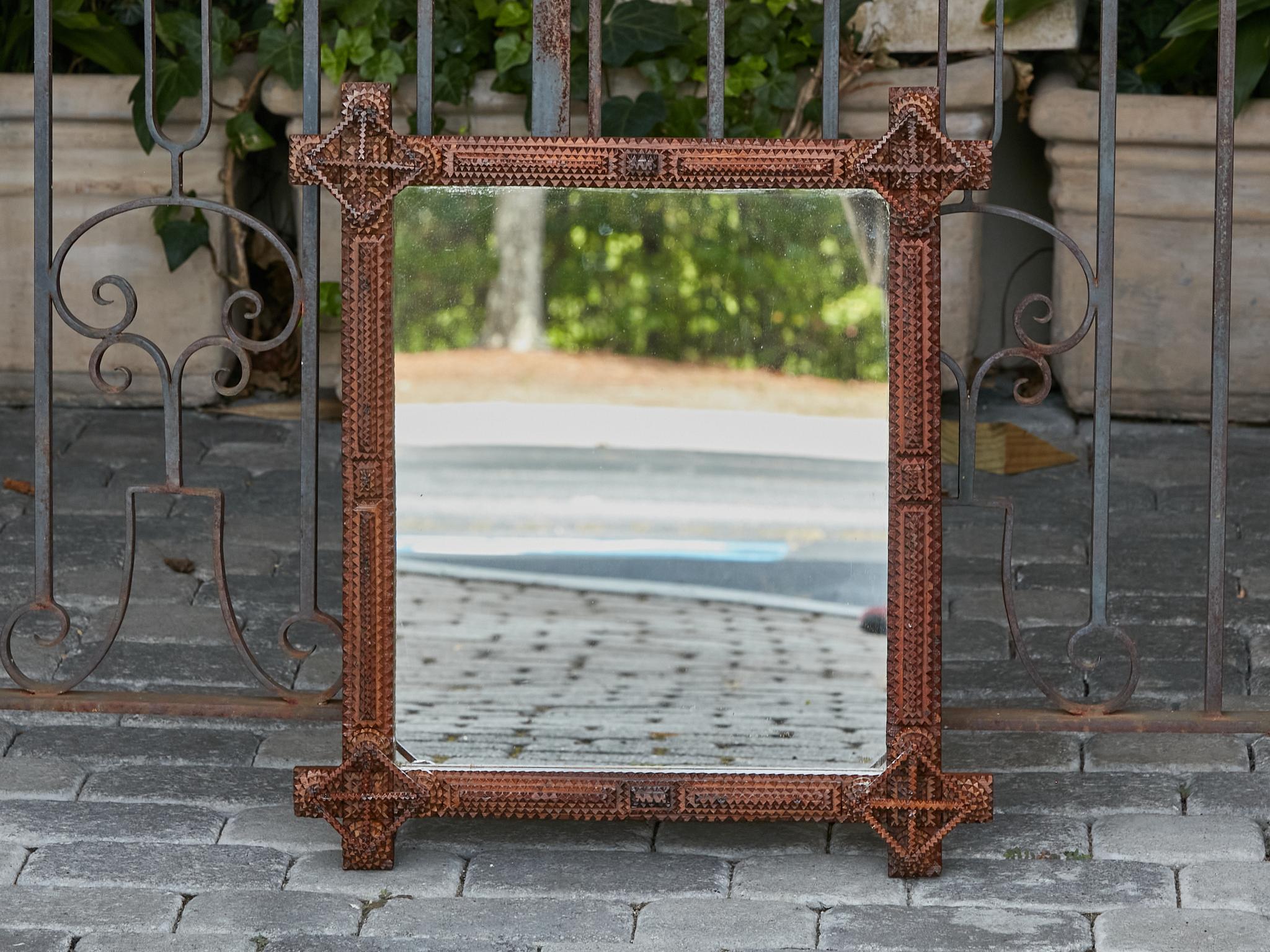 A French Tramp Art mirror from circa 1900 with carved geometric grooved motifs. Behold a striking French Tramp Art mirror, meticulously crafted circa 1900, that serves as a tangible connection to a bygone era of exceptional artistry. The frame is