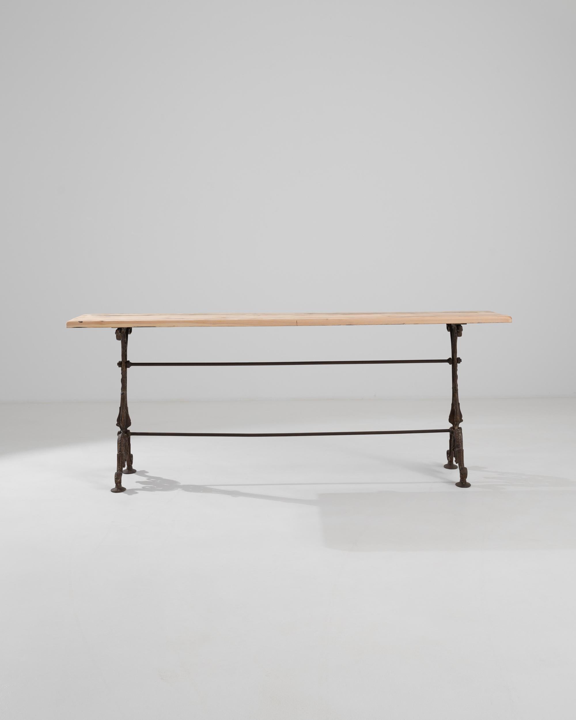 Slender and elegant, this vintage table makes a unique and versatile accent. Made in France at the turn of the century, a narrow rectangular tabletop in natural wood sits atop an elaborate cast iron base. Recalling the decorative Belle Epoque