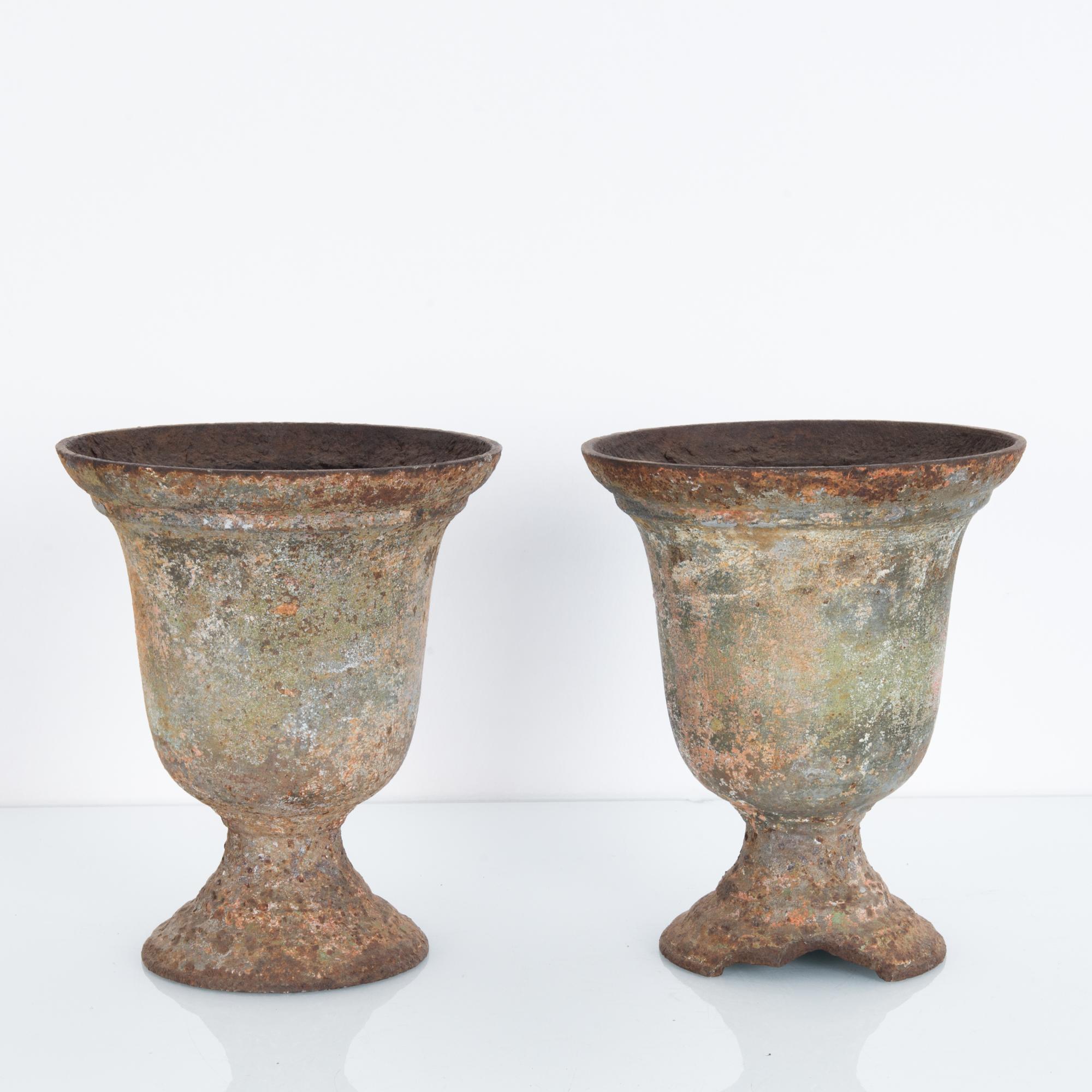 A pair of cast iron planters from France, circa 1900. A simple campana shape with an aged patina. Oxidation gives a color palette of rust tones, terracotta and verdigris. The weathering of the cast iron — including a missing portion of the base of