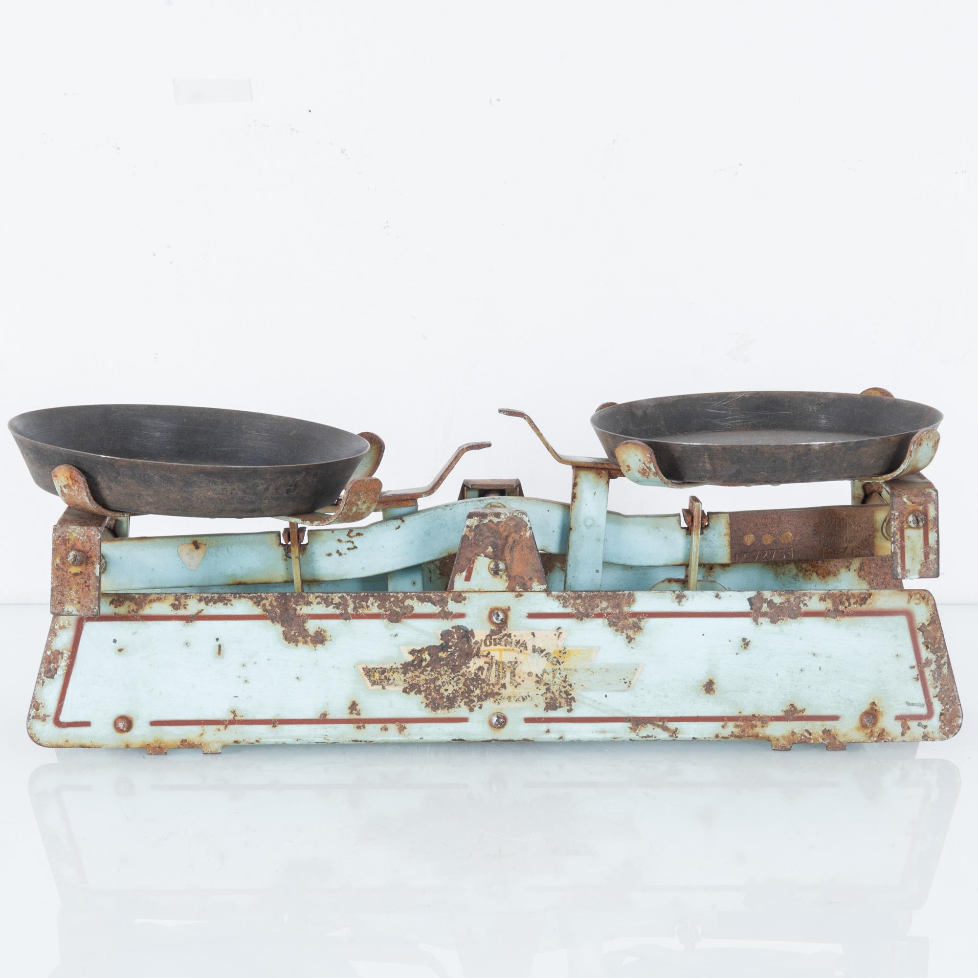 This metal balance scale was made in France, circa 1900, and brings a vintage, farmhouse accent to your kitchen. The two gray pans rest on a distressed stand painted pale turquoise. Traces of the logo are visible beneath the weathered sections.