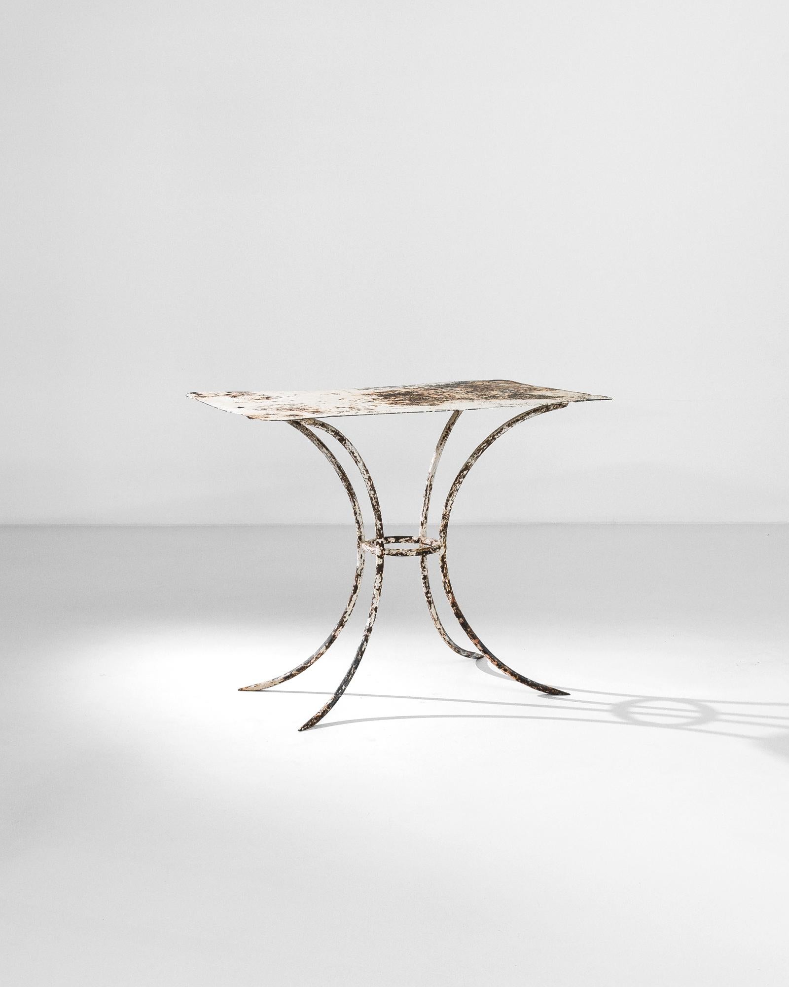 A metal table from turn of the century France with an evocative patina. Fit for the garden, rectangular tabletop with rounded corners sits atop slender legs; the parabolic curve mimics the organic growth of plant stems. The original white painted