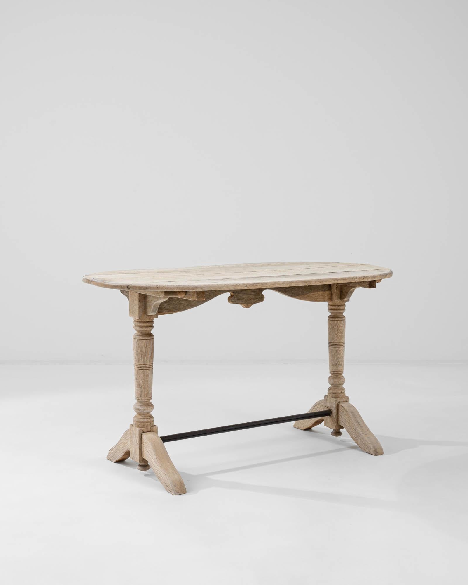 A wooden table from France, circa 1900. This small trestle table is composed of two legs with arching diagonal feet, braced by a metal rod to reinforce the time tested surface. The compact form is adapted to the necessities of bustling cafés and
