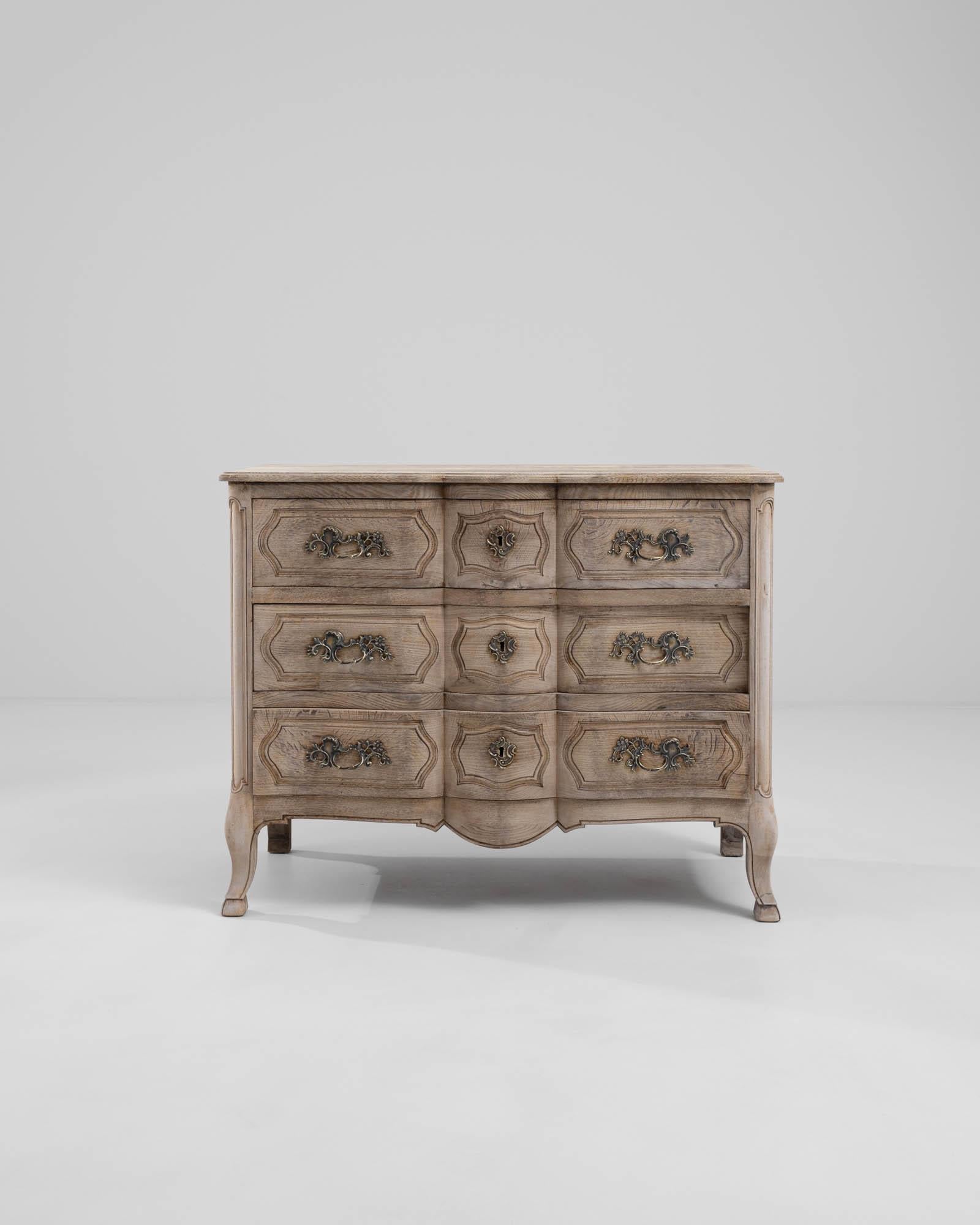 A wooden chest of drawers made in early 20th century France. The elegantly shaped, cast metal drawer pulls and key slots that adorn the front-facing sides of this exquisite chest exude a flair for panache, situated within an otherwise restrained and