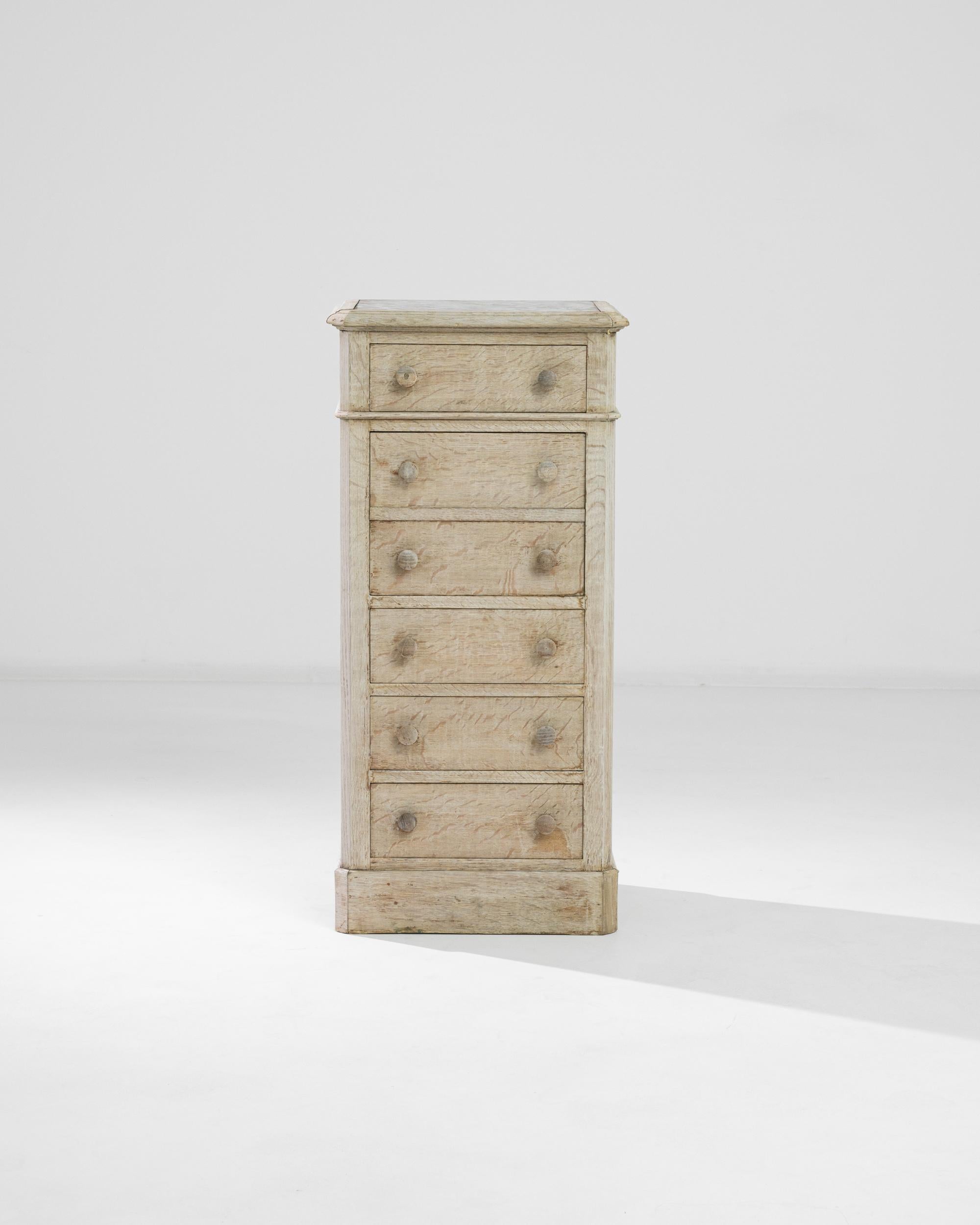 A chest of drawers in natural oak, crowned with a square of marble. Made in France at the turn of the century, the narrow silhouette has a country simplicity, accentuated by the pale, sunlit tone of the restored wood. The sophisticated red and grey