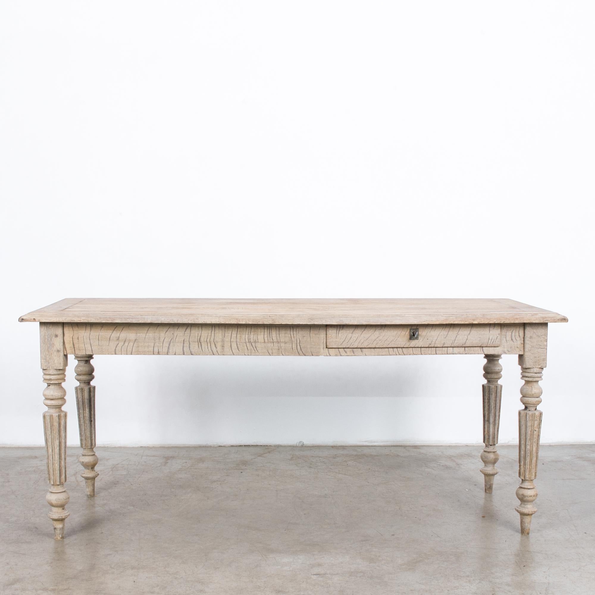 An oak dining table from France, circa 1900. A broad tabletop sits atop a square apron with a small pull out drawer, closing with lock and key. Turned and fluted legs taper down to a graceful point. The oak has been restored to a light finish,