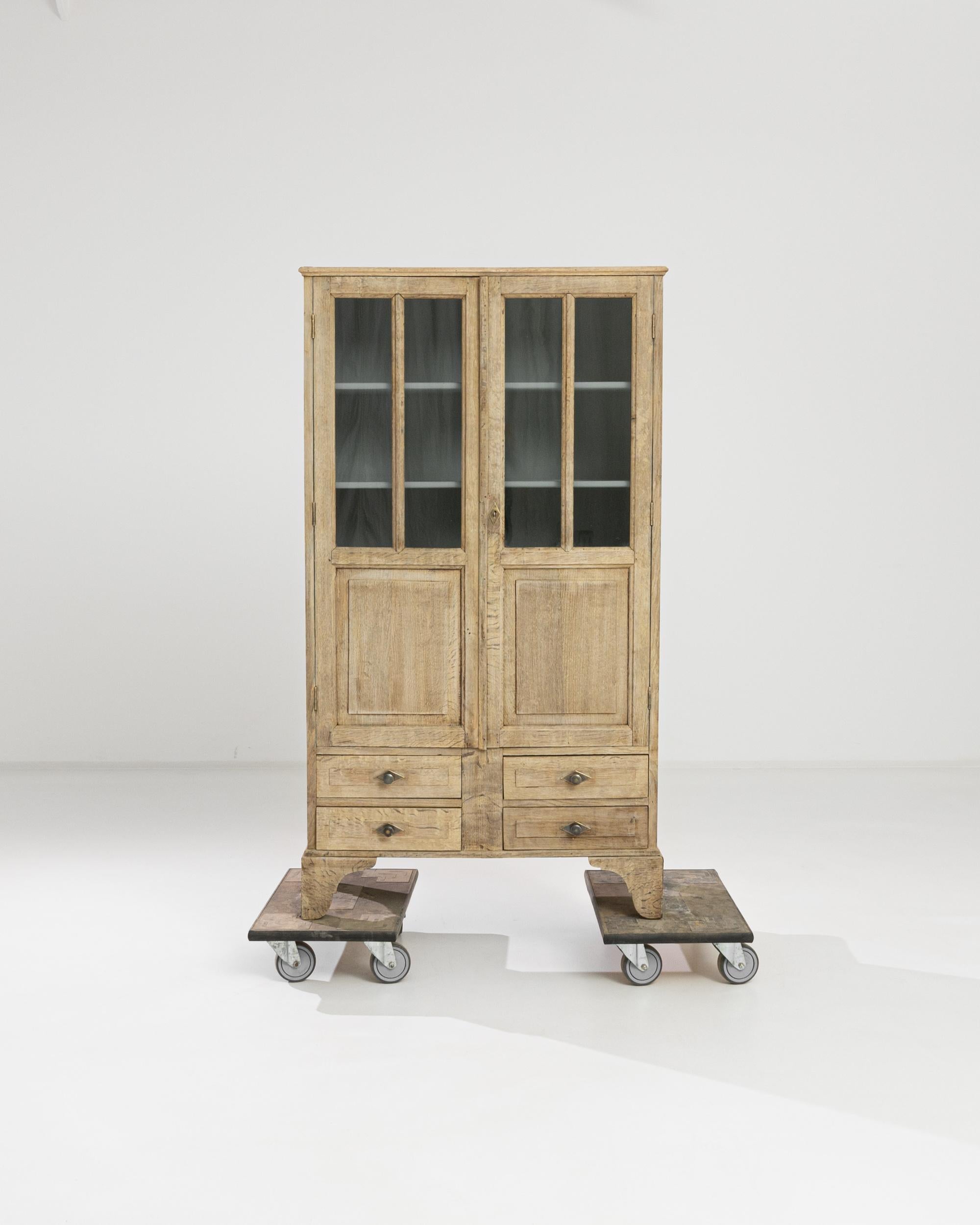 An oak vitrine from turn of the century France with a refined country aesthetic. The golden cornfield tone of the restored oak creates a warm, organic impression. The window panes of the upper cabinet peep onto interior shelves, painted sea-foam