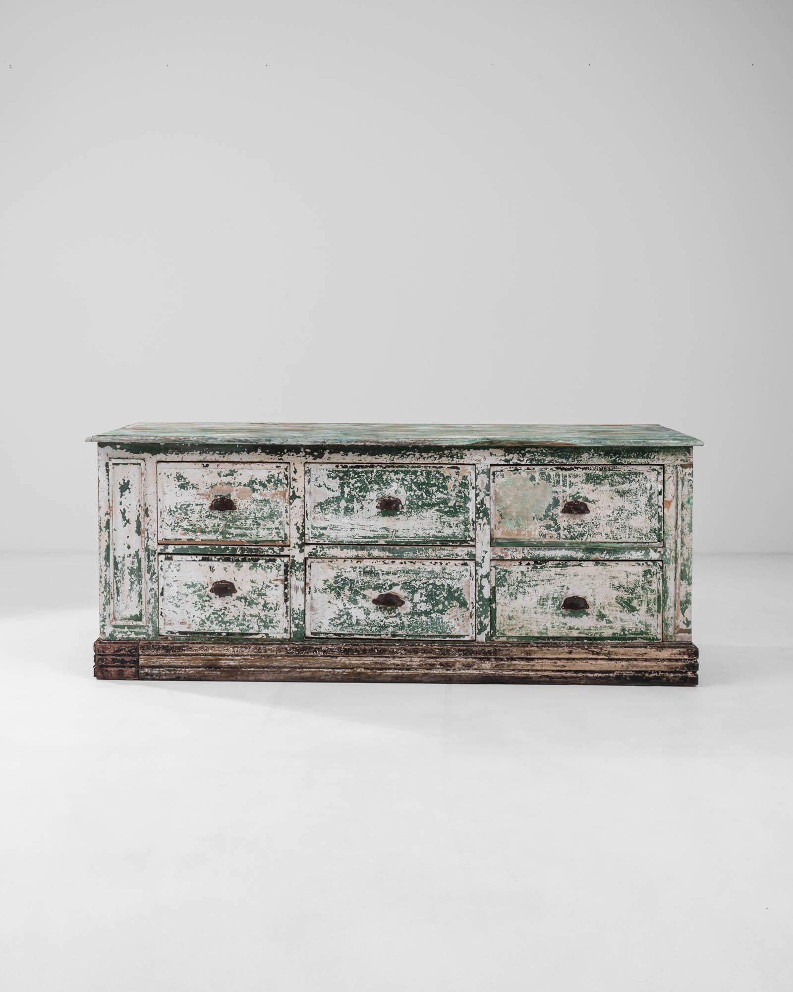The striking contrast between its orderly composition and lively, textural patina gives this vintage wooden chest of drawers a unique and compelling personality. Built in France at the turn of the century, the broad cabinet houses six deep