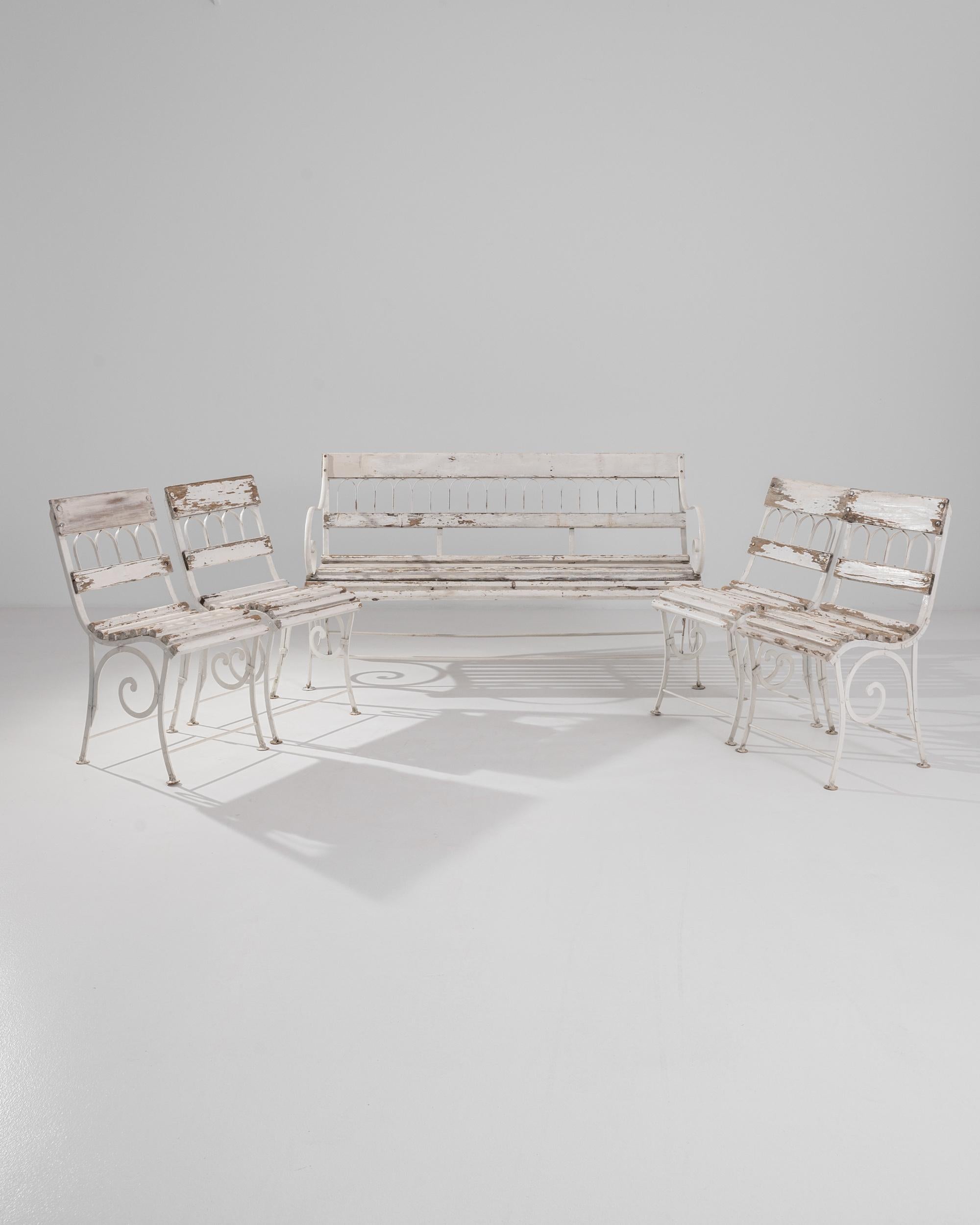 An early 20th century bench and set of four armchairs from France. Brilliant and bright wood tones shine between the cracks in a patinated cream-white coat of paint. Arching metal seat backs and spiraling leg braces suggest a refined taste, affected