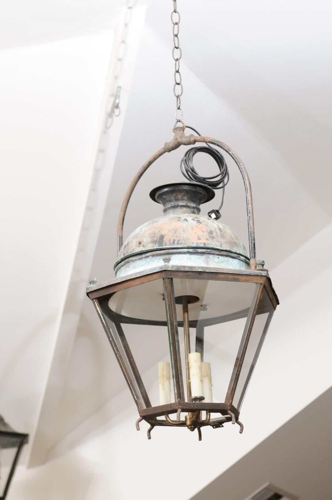 A French Provençal copper and iron hexagonal lantern from the early 20th century, with three lights and glass panels. Created in Southern France at the Turn of the Century, this lantern features a copper dome with verdigris patina, sitting above an