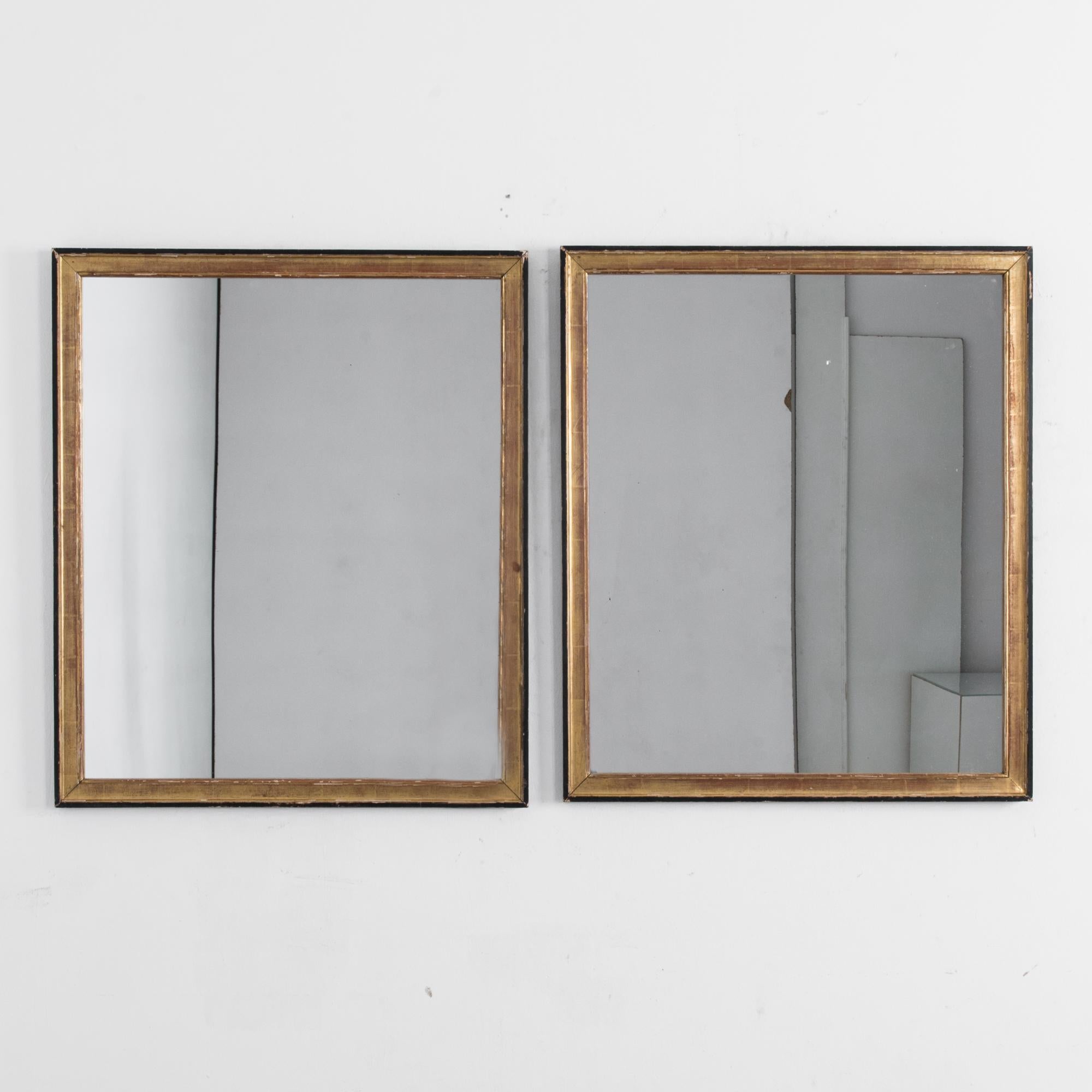 A pair of mirrors from France, circa 1900. A thin rectangular wooden frame creates a clean, sharp outline. The frame is gilded and the outer edges are painted black, creating a stylish contrast. A gentle patina softens the painted surface of the