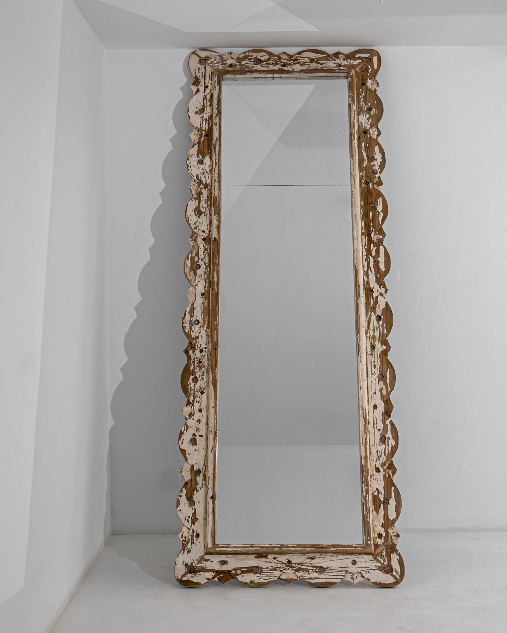 This antique wooden mirror was produced in France, circa 1900. A tall piece with a striking patina elevating over three meters, and flaunting a seasoned russet wood under a cream white paint. The frame is layered with acute and rounded shapes,