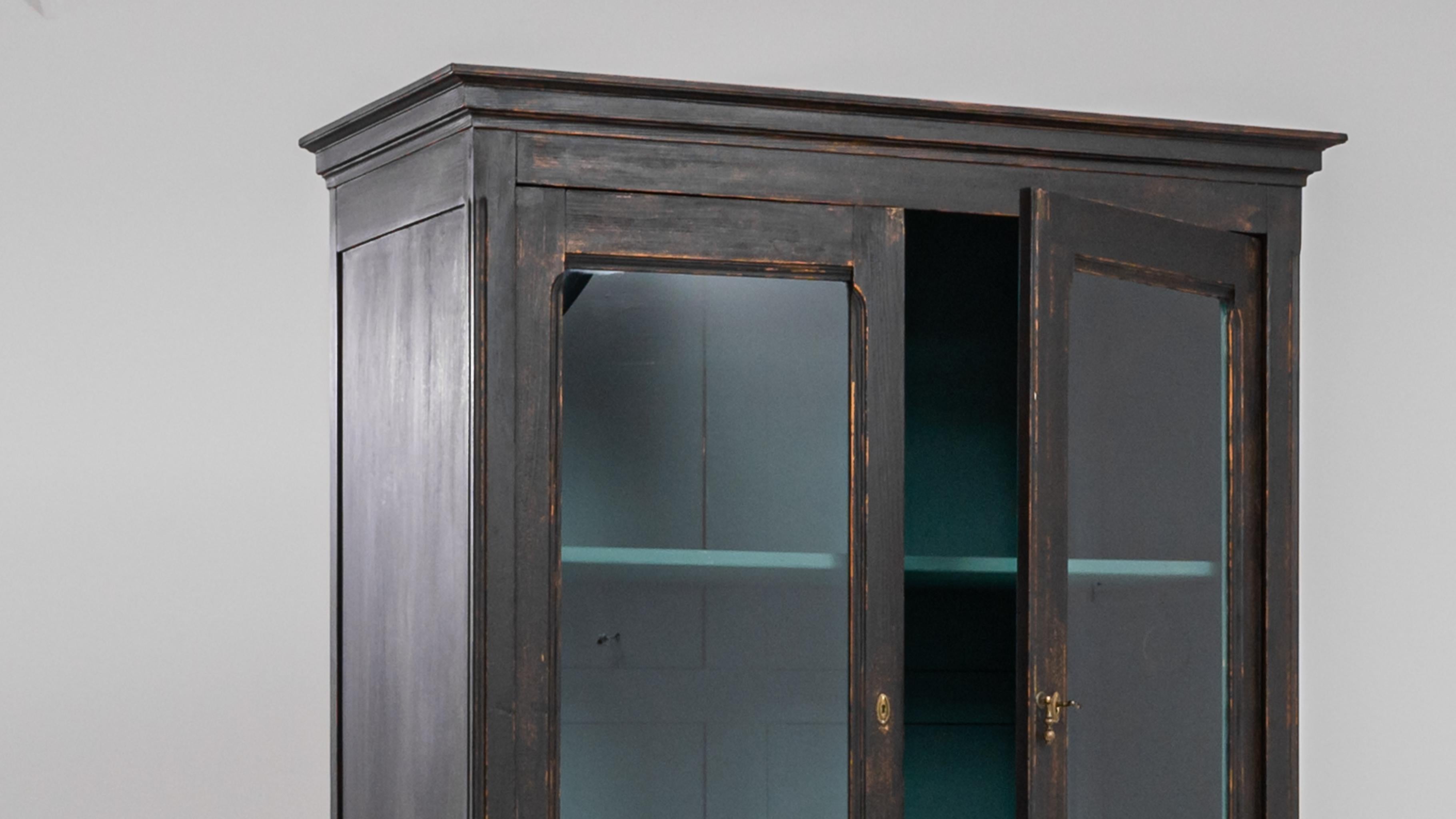 This turn of the century wooden vitrine makes a distinguished display case. Sourced from France, the sober black-painted finish has acquired a gentle patina over time, revealing glimpses of the warm cherry-colored wood beneath. Paned windows give a