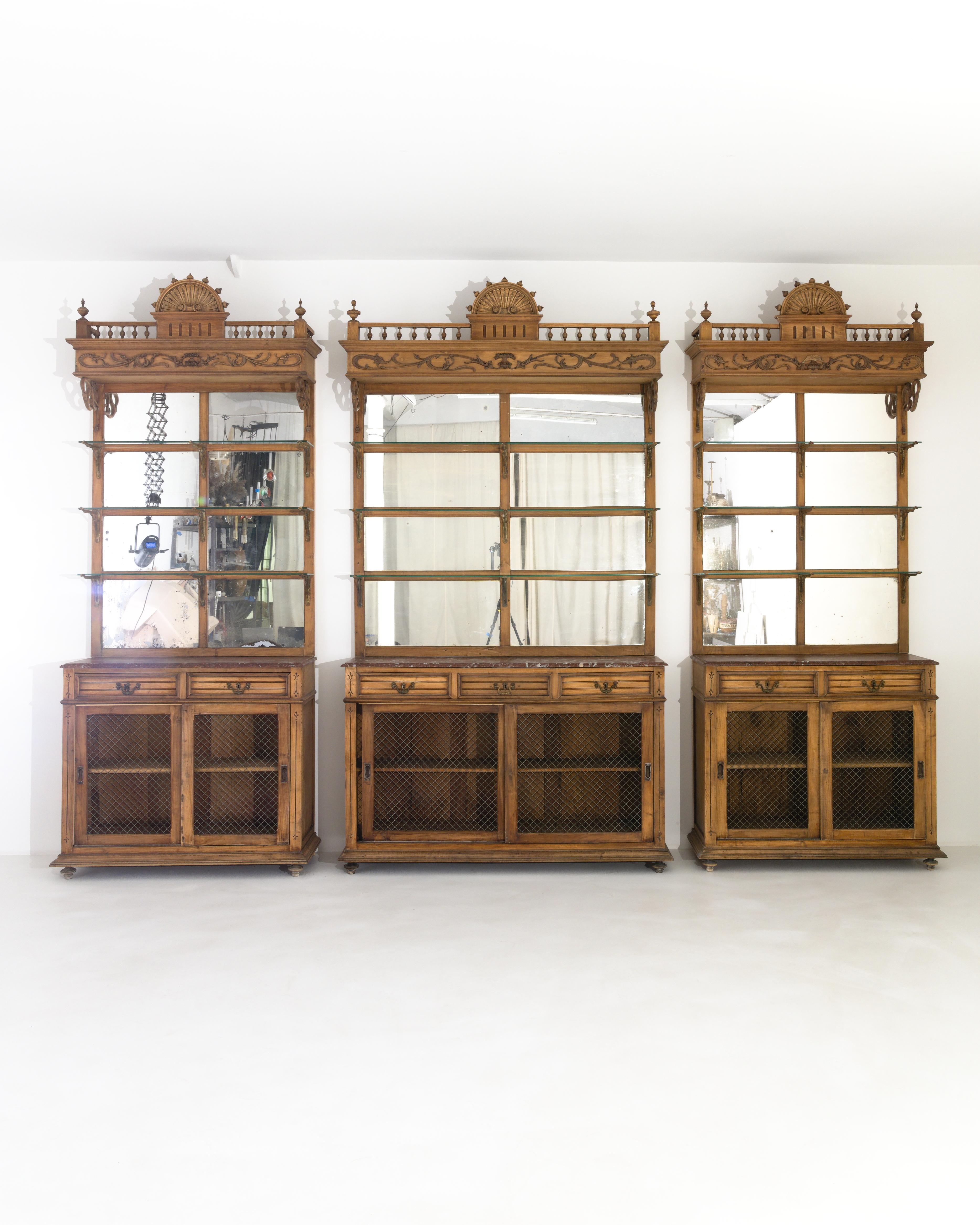 This trio of wooden display cabinets combine a variety of decorative motifs into a wonderfully eclectic design. Made in France at the turn of the century, the mirrored panes of the back panel reflect the light within the room and onto the glass