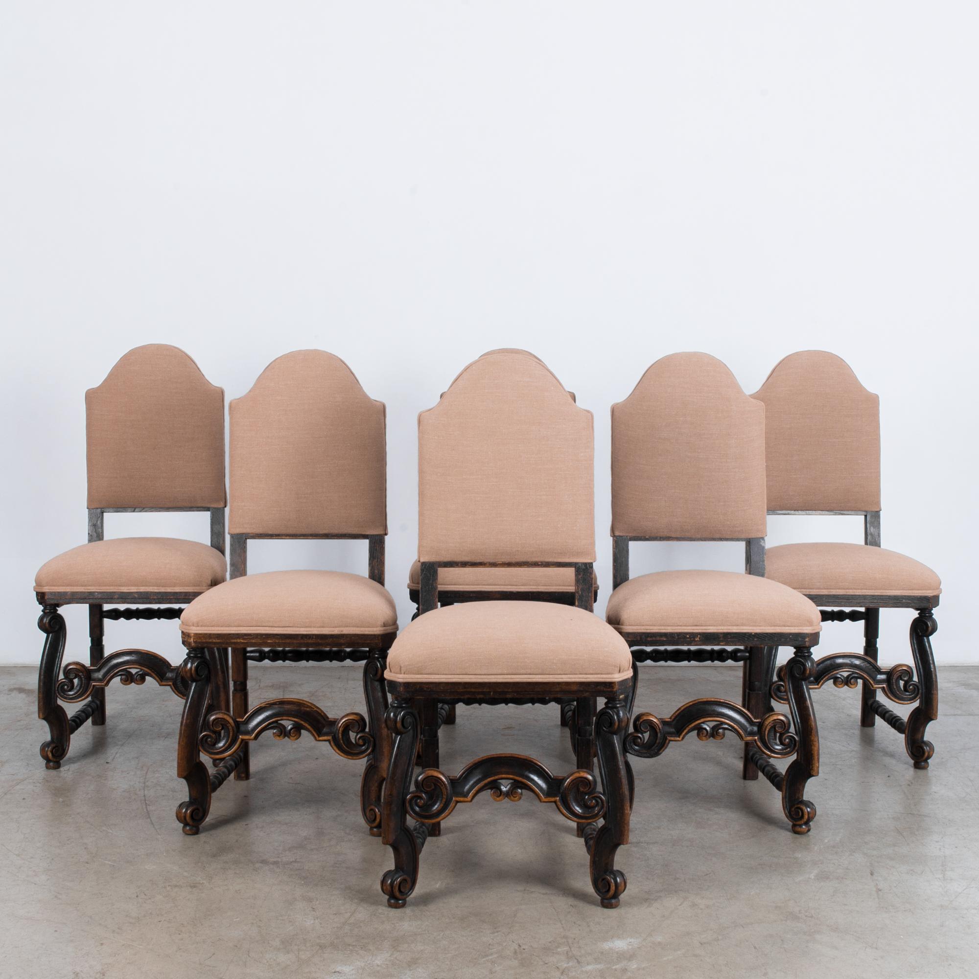 A set of six wooden dining chairs from France, circa 1900. A dark, elaborately carved frame supports an upholstered backrest and seat. The rose taupe color of the upholstery lends a soft, intimate touch to the Baroque scroll-work of the frame,