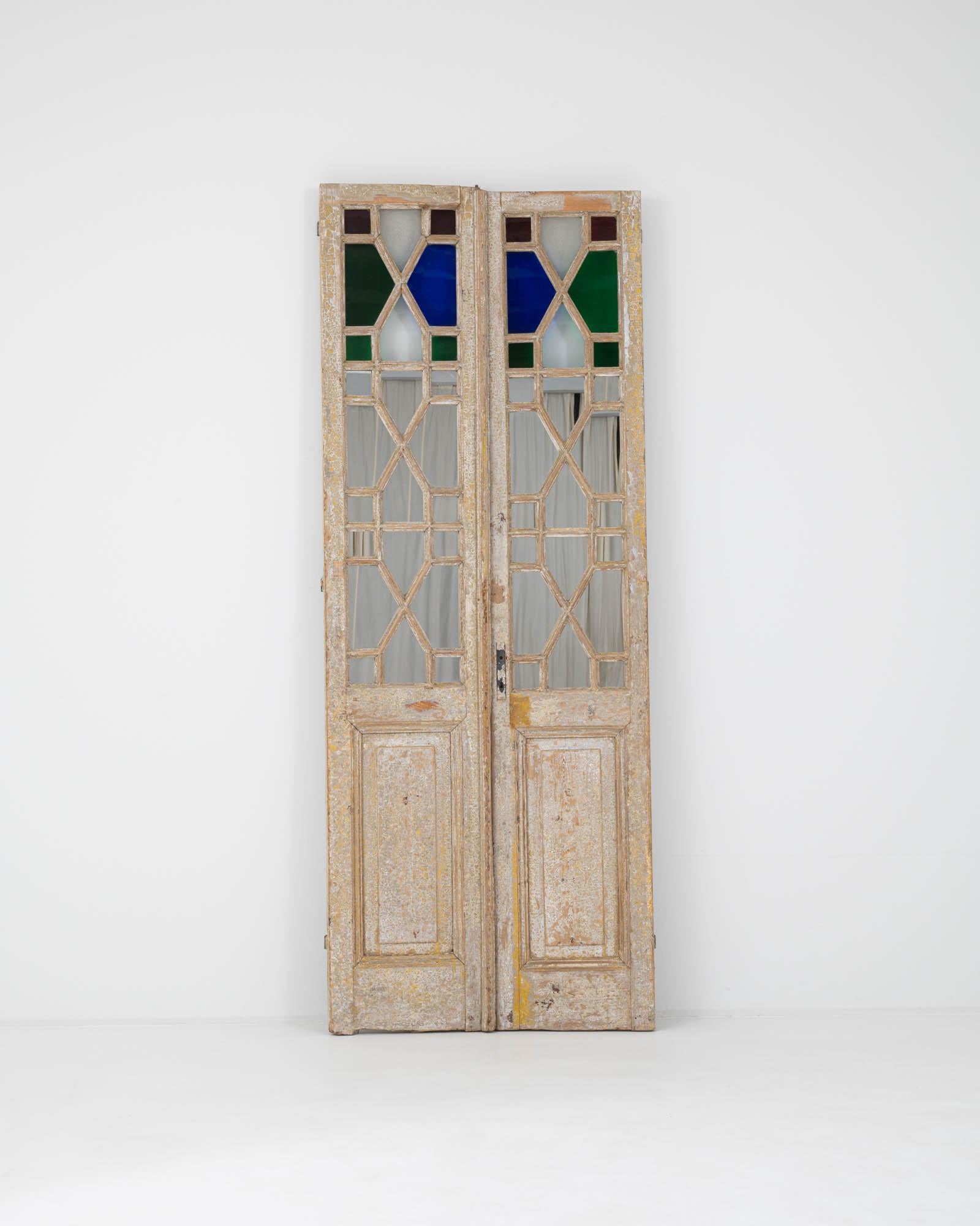Tall, slender and beautifully decorative, this pair of vintage wooden doors conjures the everyday elegance of a bygone age. Made in France at the turn of the century, the once-painted surface of the wooden frame has weathered to a nostalgic finish.
