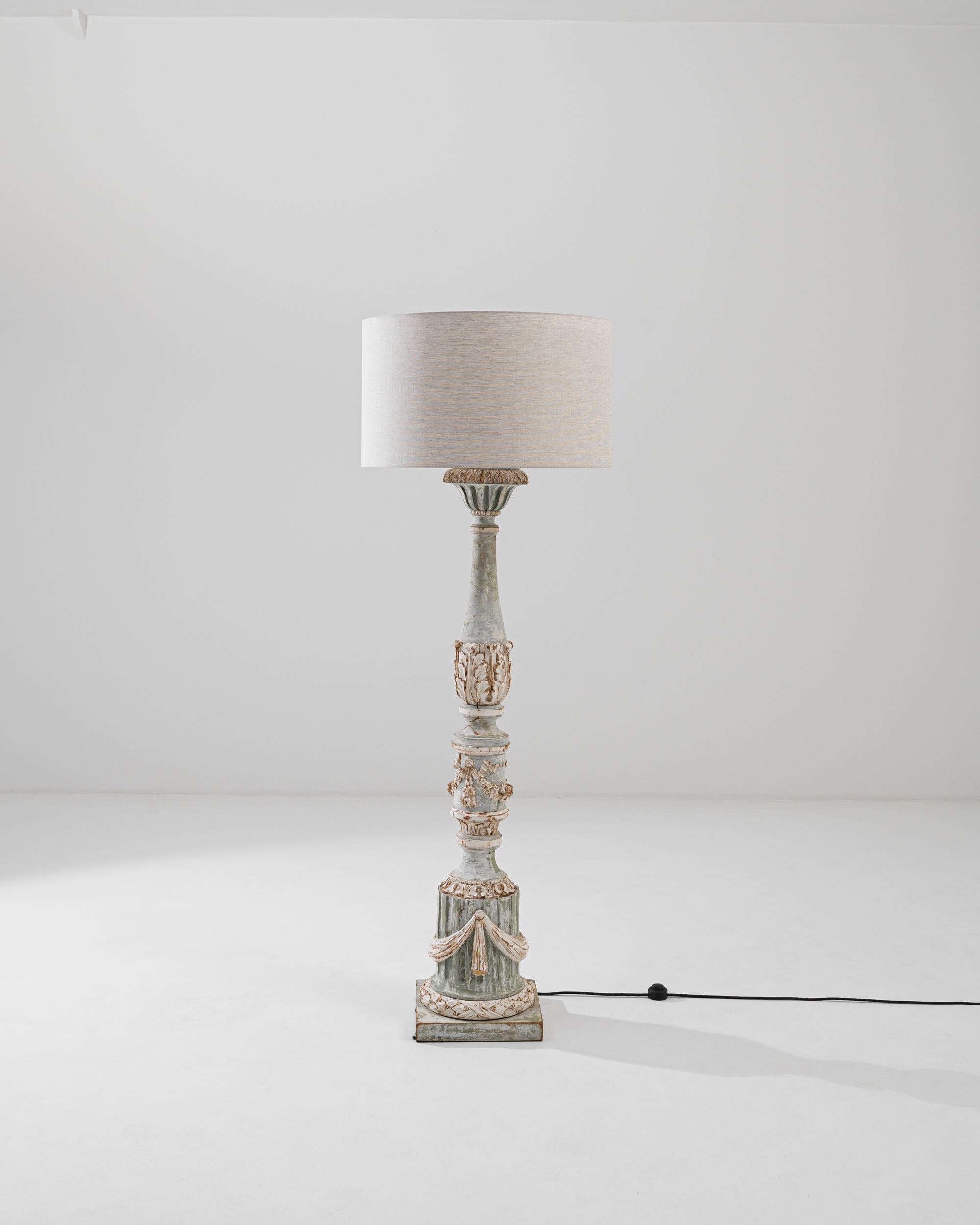 Delicate and ornate, this carved wooden floor lamp brings an element of French whimsy to an interior. Made at the turn of the century, the design offers an elaborate interpretation of Neoclassical motifs. The fluted column of the base is hung with