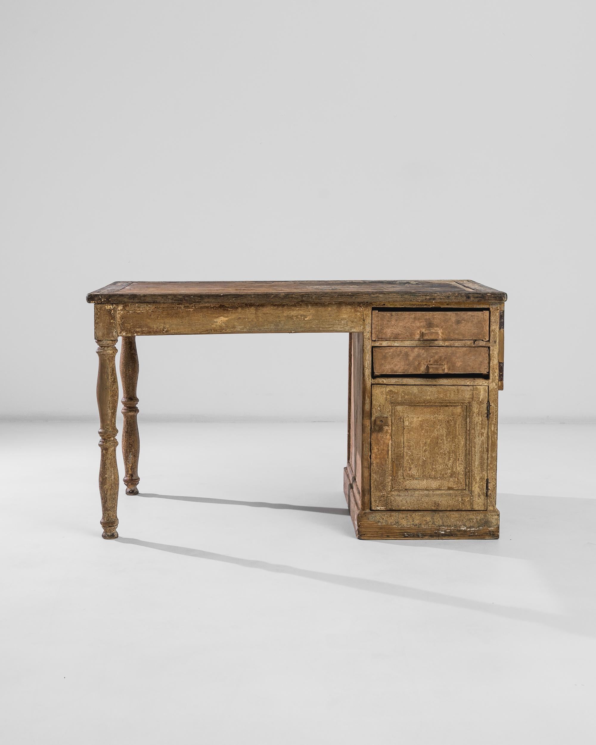 An asymmetric writing desk from turn of the century France, featuring ring turned legs and a pedestal two-drawer cabinet. The flavourful century-old patina blossoms in a myriad of honeycomb tones and nuances, flourishing in a heavy grain and