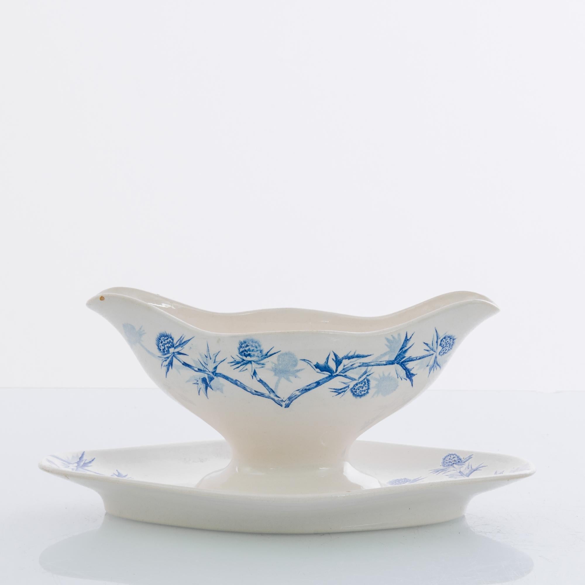 A ceramic sauceboat from Germany, circa 1900. White china is decorated with an intricate pattern of slender stems and symmetrical buds in indigo blue. The delicate contour and out-turned lip of the sauceboat suggests the shape of a tulip; beneath, a