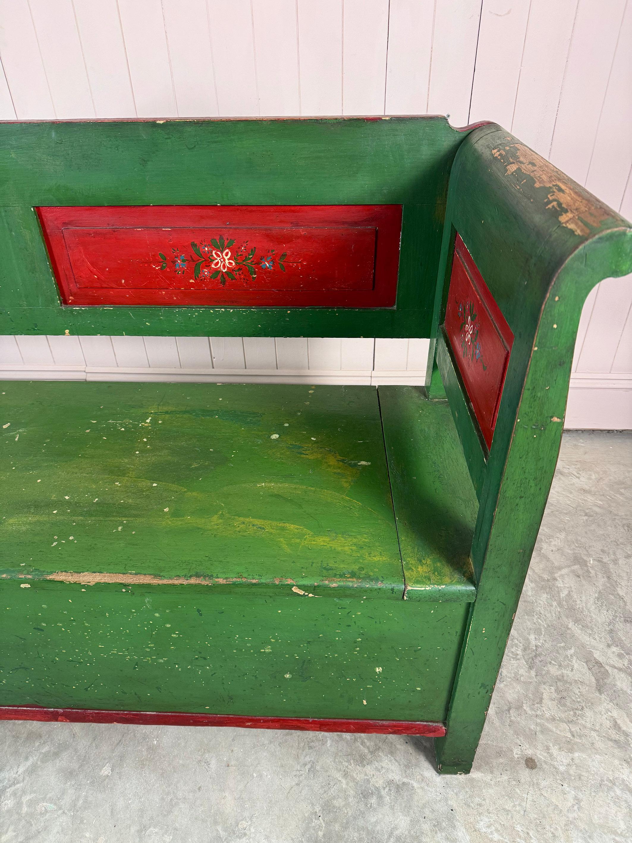 This settle or bench is early 20th Century, possibly older.  Original green and red paint full of rustic charm and an exquisite example of folk craftsmanship.  Wonderful natural colours and patina.  This bench serves a dual purpose with its seating