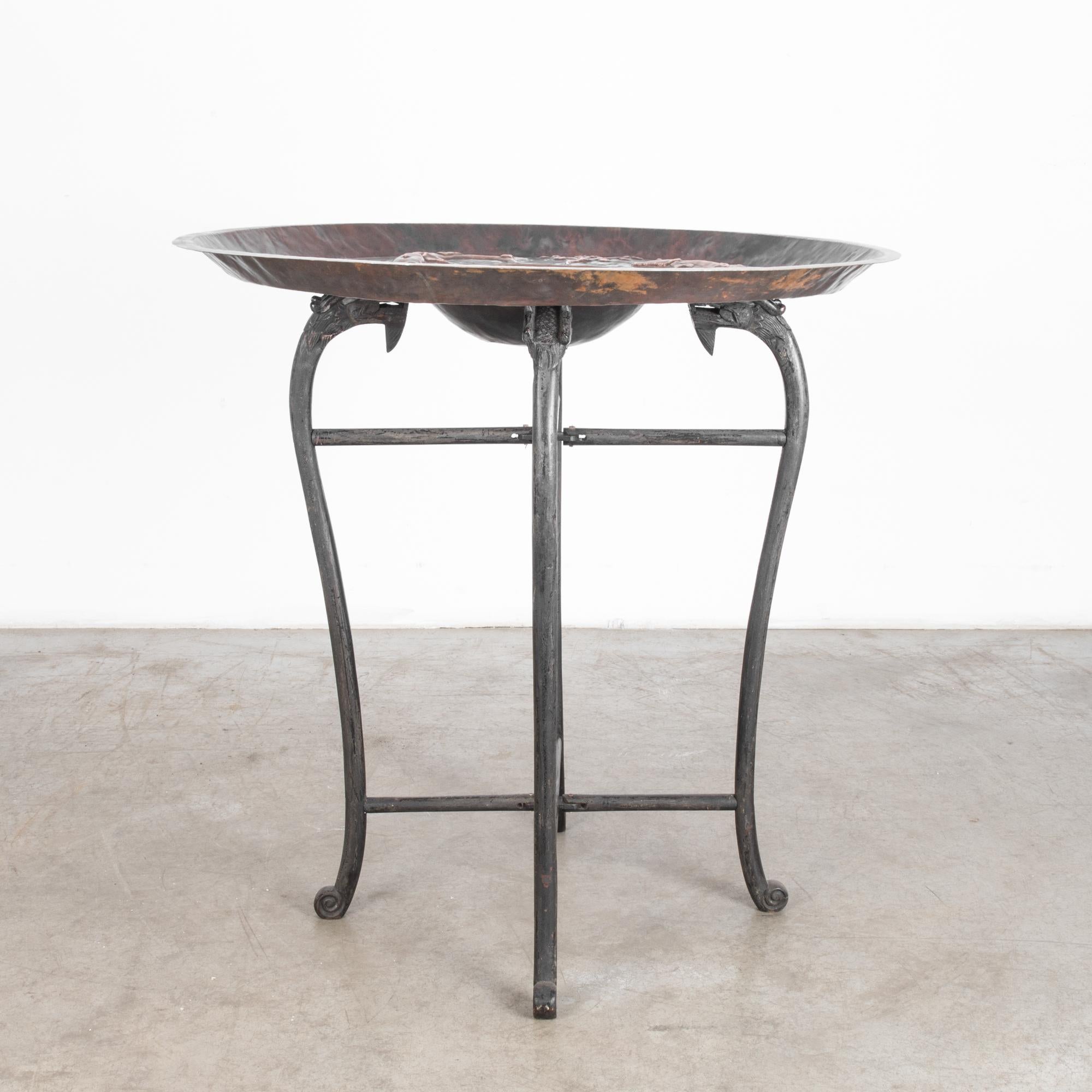 This table is composed of a deep copper tray which rests upon a carved, folding wooden stand. Made in India, circa 1900, both tray and stand feature elaborate decorative elements. The slender, curving legs of the stand, finished in a dark, burnished