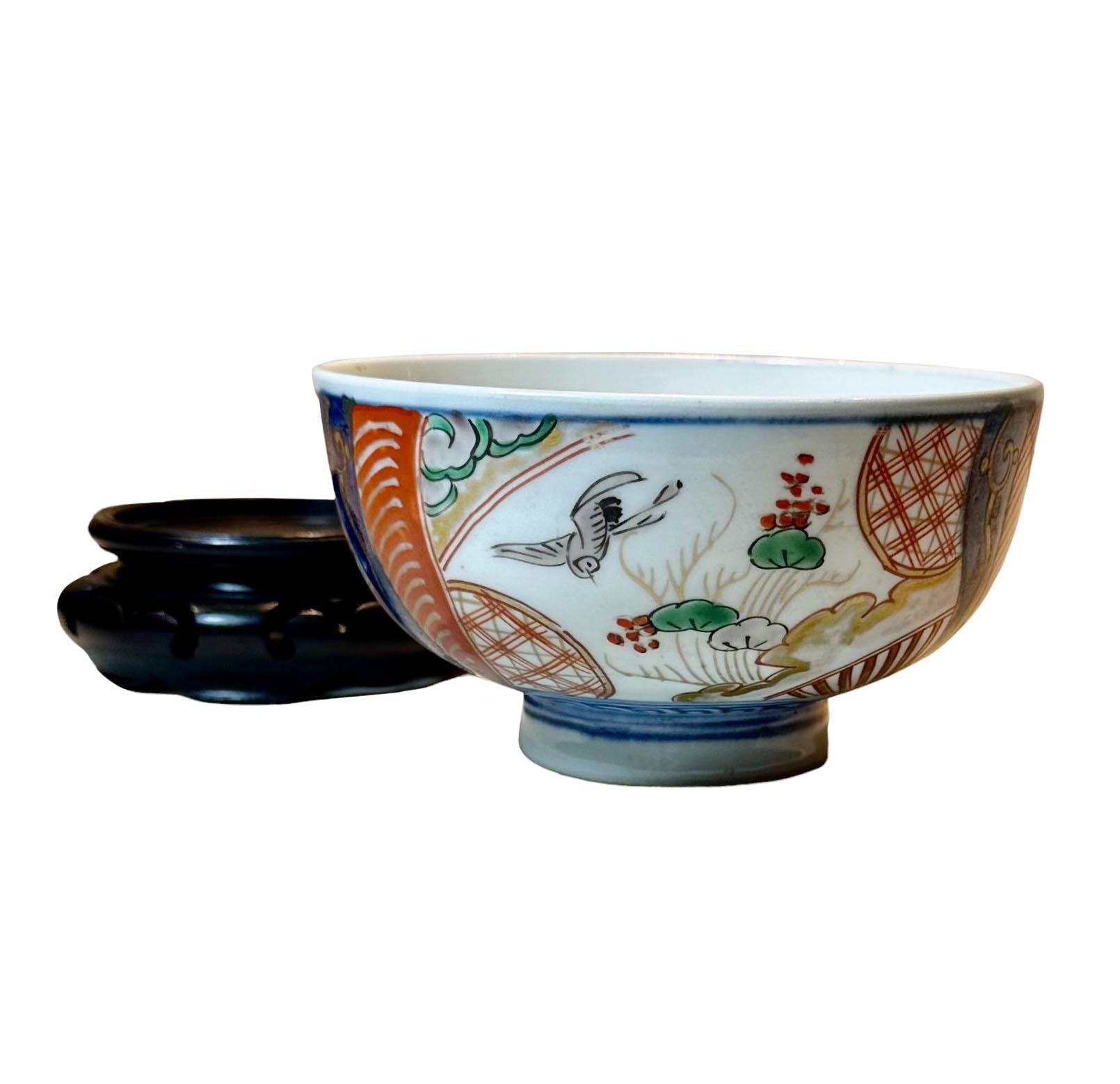 An early turn of the century Japanese Imari rice bowl on a Chinese wooden stand. The bowl is two and a half inches high and the stand is an inch high.