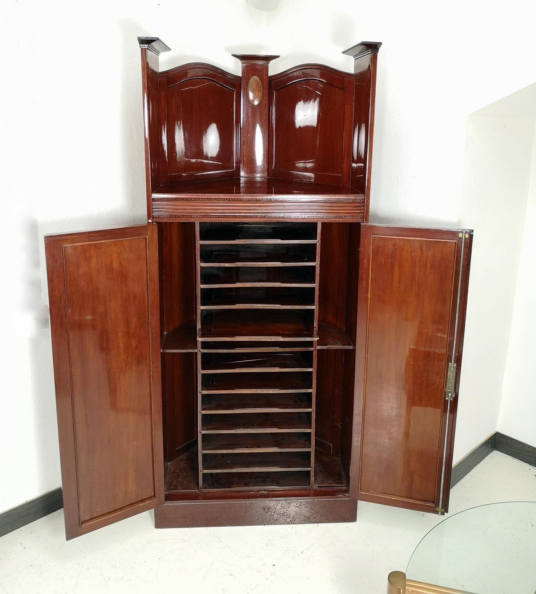 This large corner cabinet features two opening doors with twelve shelves inside. With harp and lute inlay, this turn of the century mahogany corner cabinet with inlayed intarsia has its original working lock. Fully restored, with handmade French