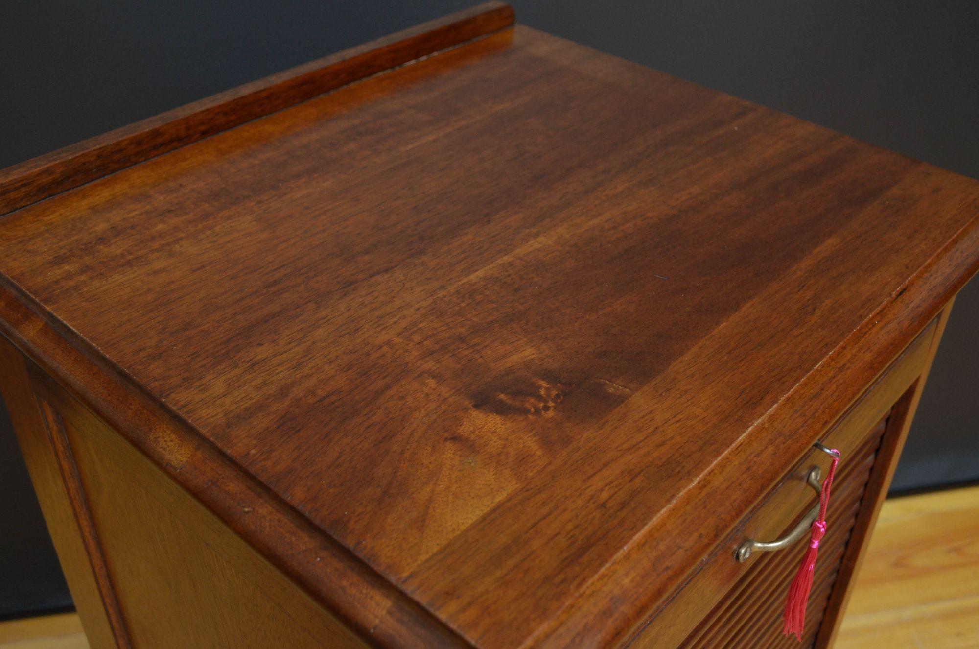Sn5348 Early 20th century mahogany, tambour fronted filing cabinet, having shaped upstand to moulded top, panelled sides and tambour front enclosing nine drawers, all fitted with original working lock and key, standing on plinth base. This antique