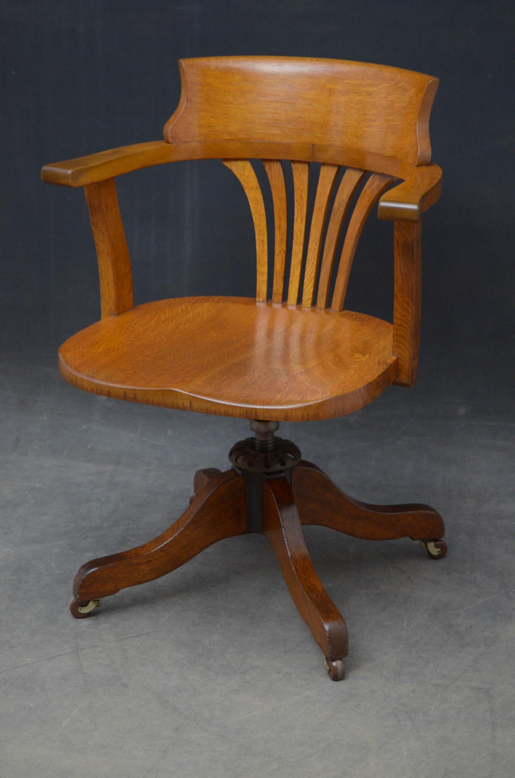 Sn5036, elegant revolving desk chair in oak, having shaped top rails with six splats below, open arms and generous seat, raised on revolving mechanism with four shaped legs terminating in brass castors. This antique chairs has been syamthetically