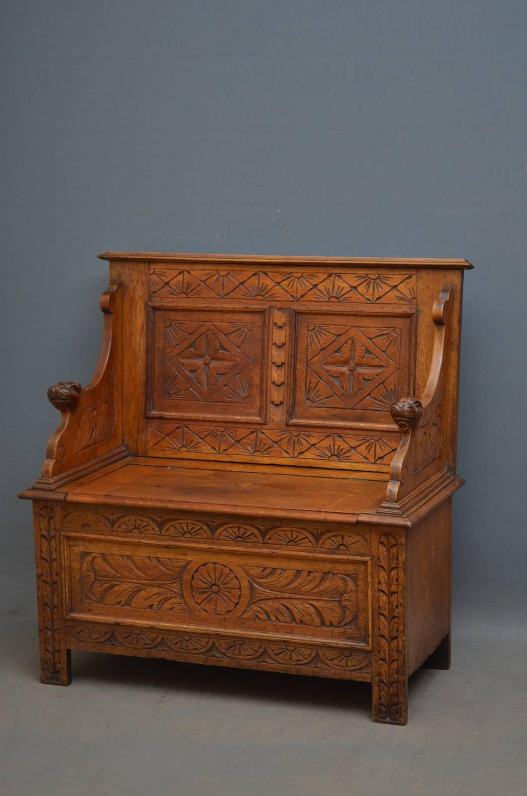 K0304, turn of the century oak bench of small proportions, having carved and panelled back, hinged seat enclosing a storage compartment, carved arms and panelled and carved base. This antique hall bench retains its original finish, color and