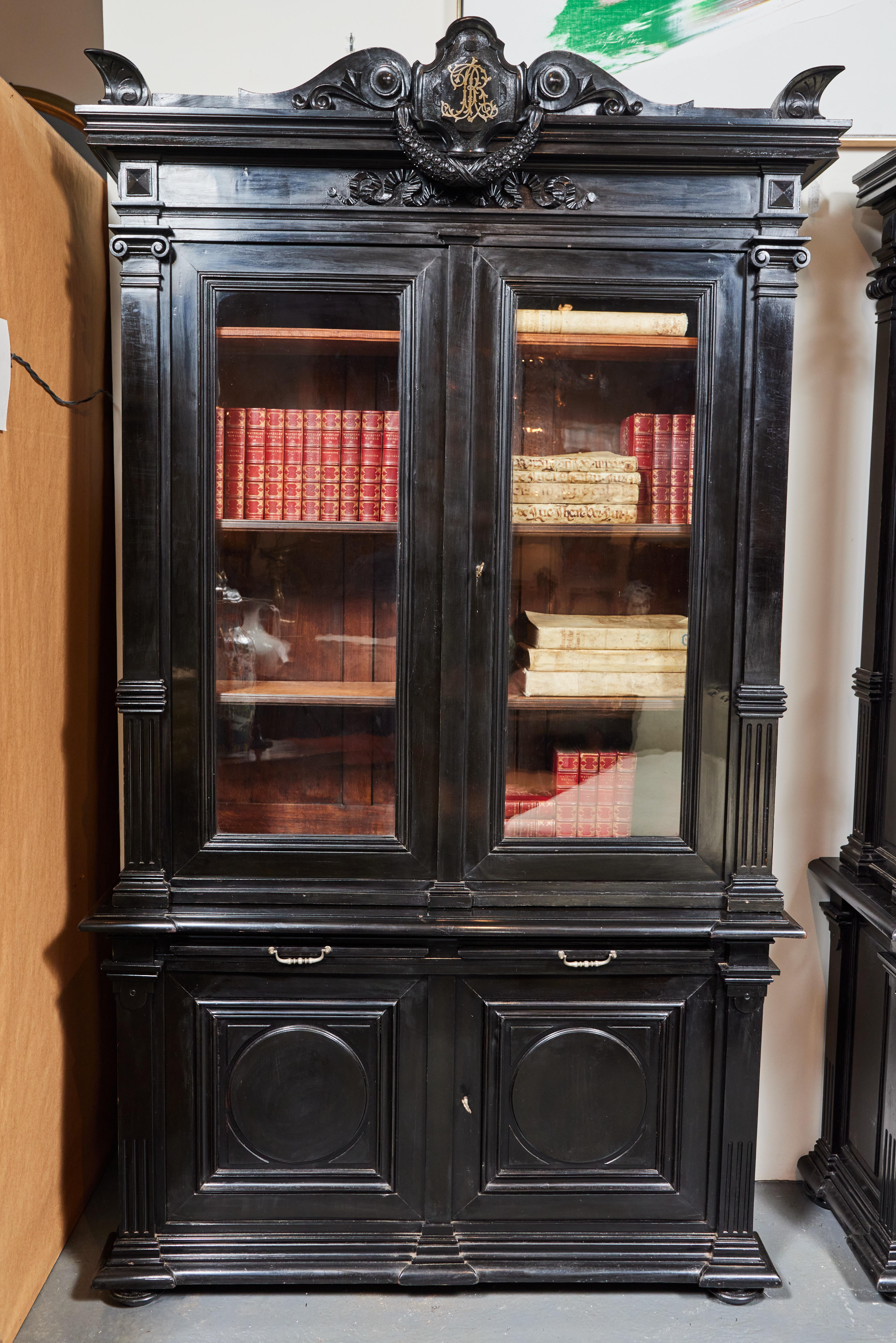 A substantial, rare pair of mated, hand-carved, ebonized, turn-of-the-century, two part Italian bookcases. Each with glass front doors bordered by fluted, faux pilasters rising to Ionic capitals supporting an entablature featuring a stunning