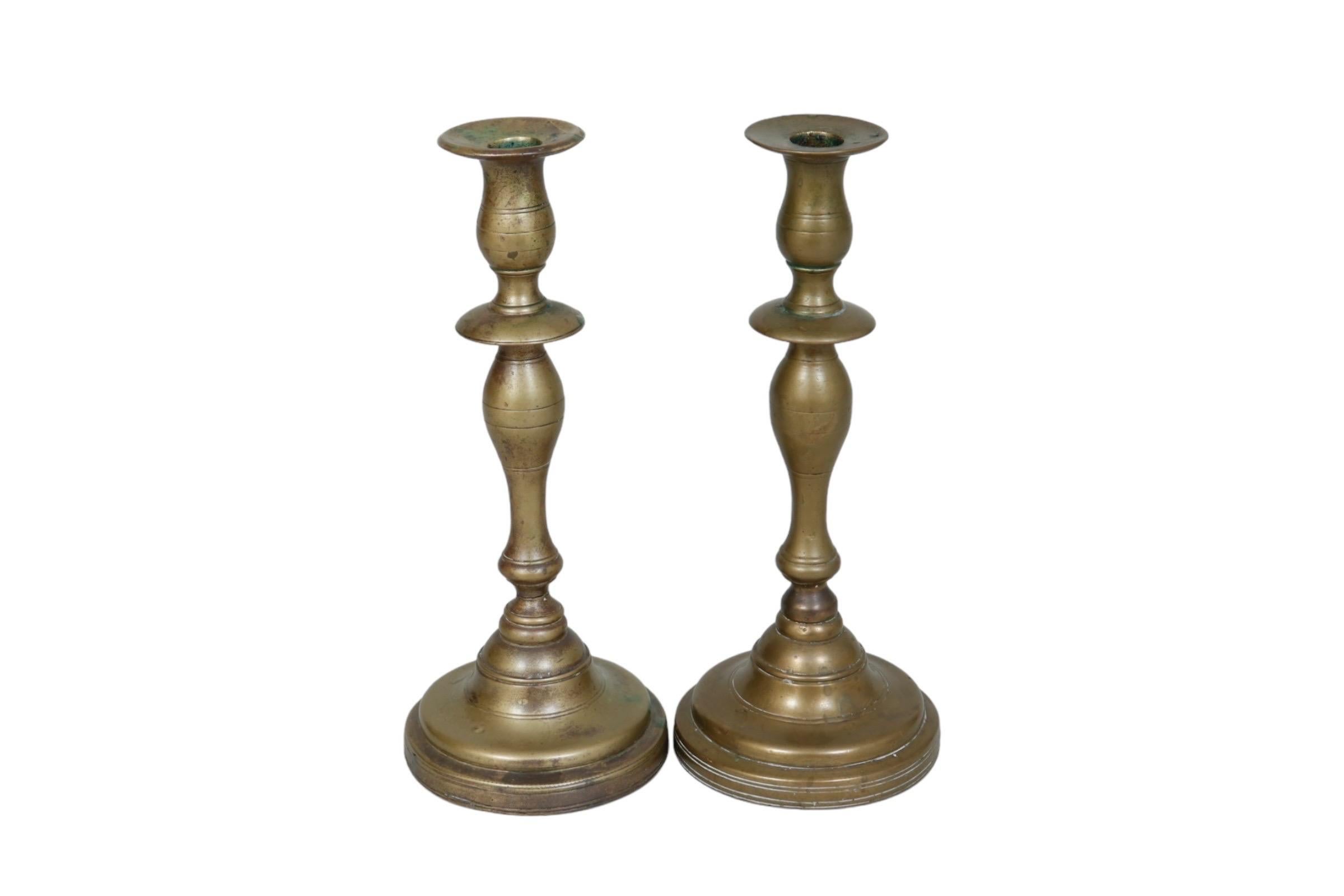 Una coppia di portacandele tradizionali torniti in ottone. Semplici colonne a balaustro sono tornite con eleganti padelle e spalle in cera sopra basi rotonde. Dimensioni per portacandele.
