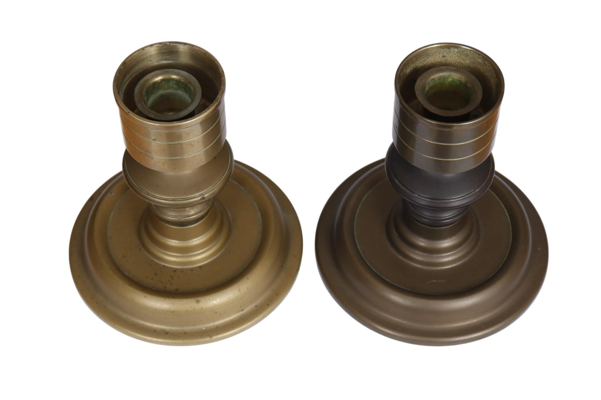 A pair of turned brass chamber stick candle holders. Turned with decorative beveled lines on the capital above a single knop on the stem. Beveled wells top round bases. Dimensions per candle holder.
