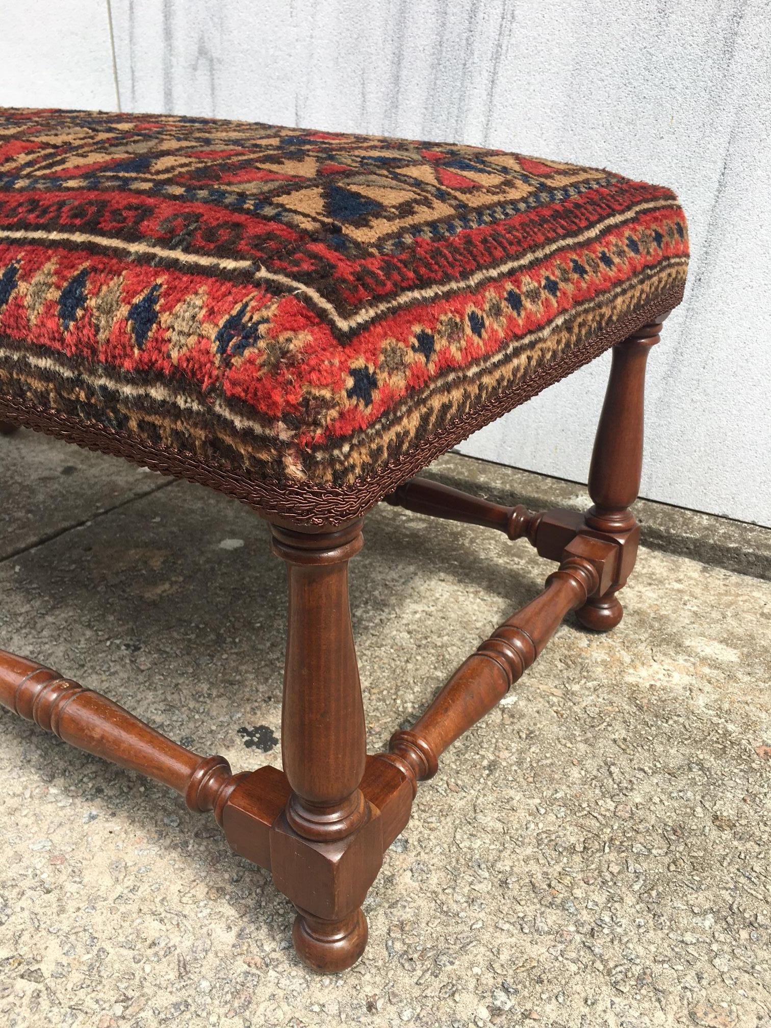 Questa bella panca in legno tornito è ricoperta da un suggestivo tappeto da preghiera del Balochistan tessuto a mano. Caratterizzato da un motivo geometrico in colori deliziosi, questo pezzo può fungere da tavolino o da poggiapiedi lungo.  Mogano