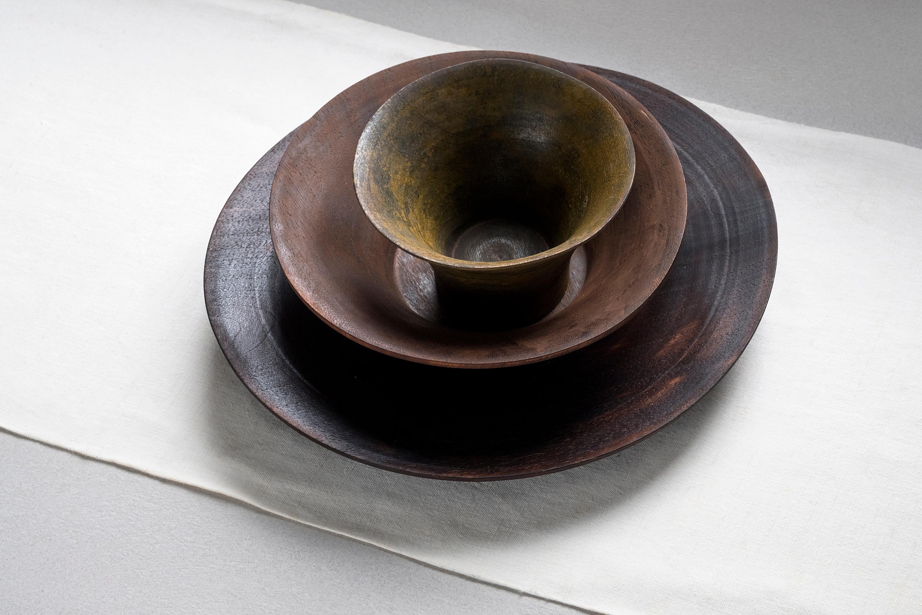 Coral is a set of irregular plate and bowls, masterfully turned with thin thicknesses. The three pieces are made of walnut wood, colored by finishes starting from metal oxides, that twist the material’s perception of the object. This table set is