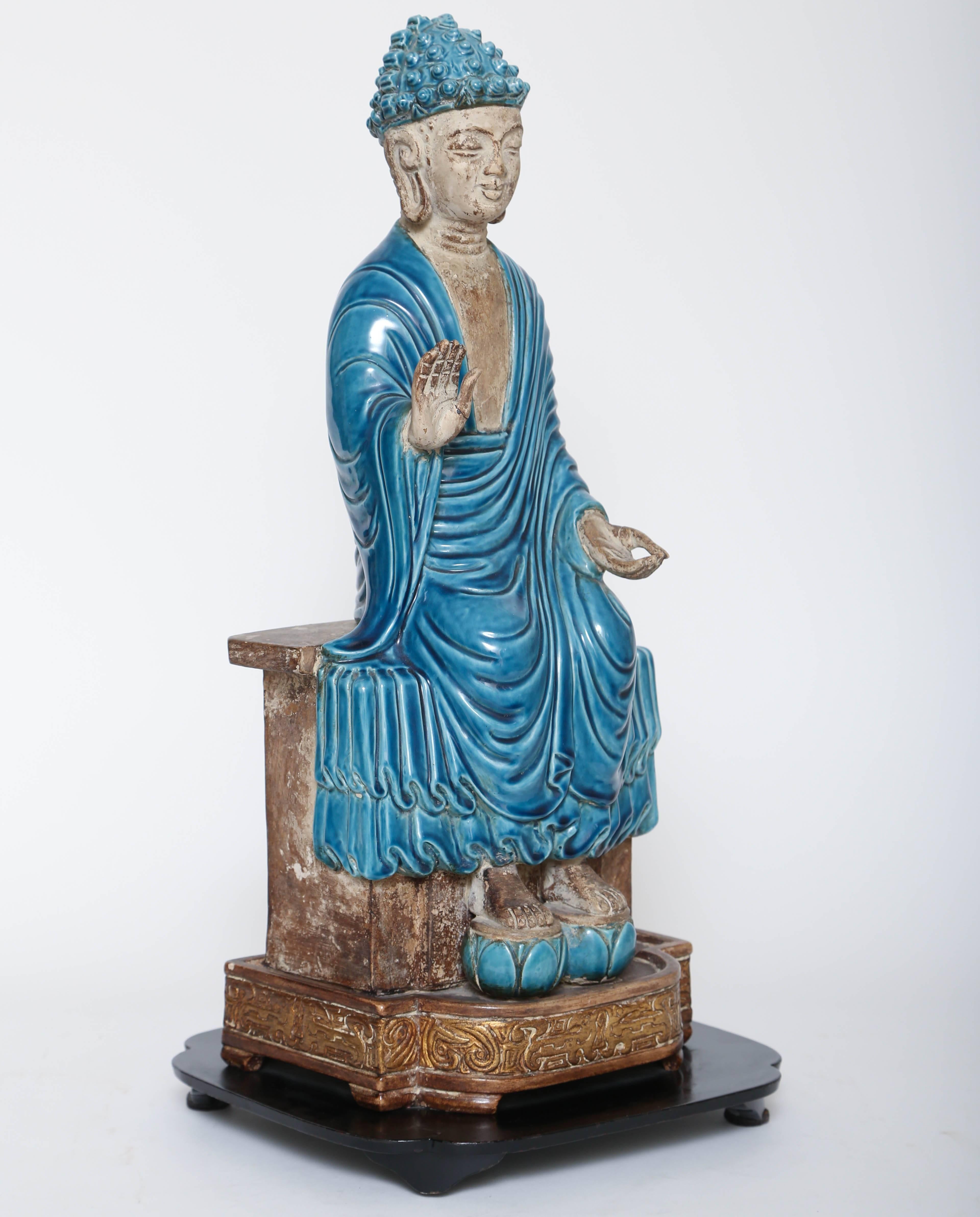 Decorative terracotta Buddha with turquoise accents on gilt and ebony base.