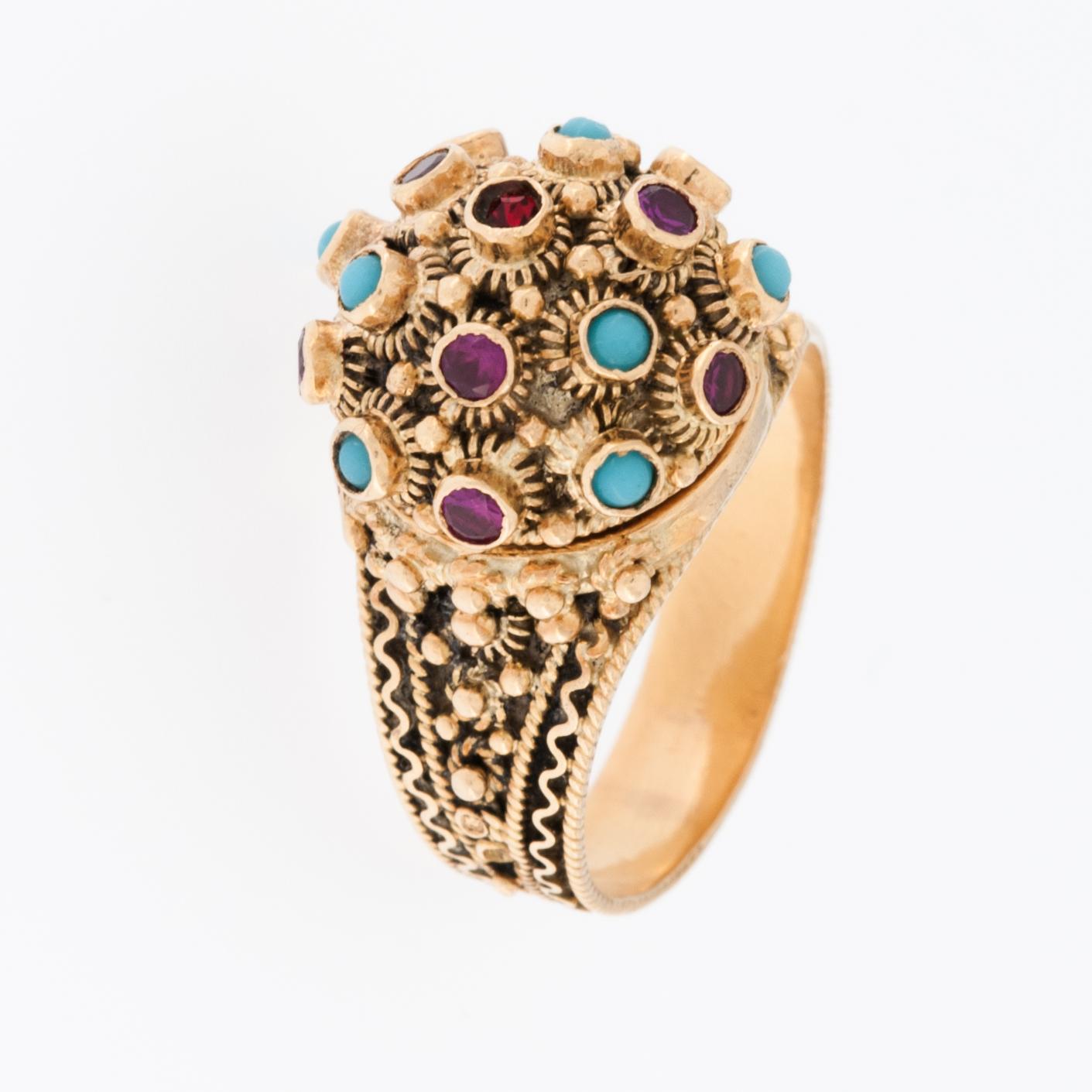 Der Türkis- und Rubinstein-Ring aus 19 Karat Gelbgold ist ein atemberaubendes, seltenes und aufwändig gearbeitetes Schmuckstück. 

Türkis ist ein Halbedelstein, der für seine schöne blaugrüne Farbe bekannt ist und oft mit Ruhe und Schutz assoziiert