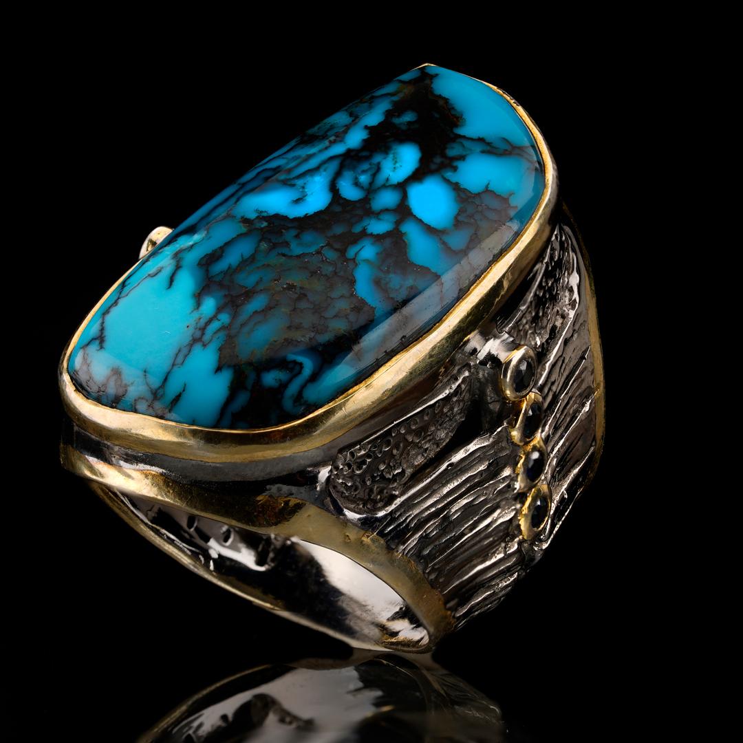 The large hand-polished specimen of natural turquoise on this statement ring features incredibly saturated blues. Swirled with ink-like inclusions for a unique, painterly aesthetic, the turquoise is set in sterling silver and accented on either side