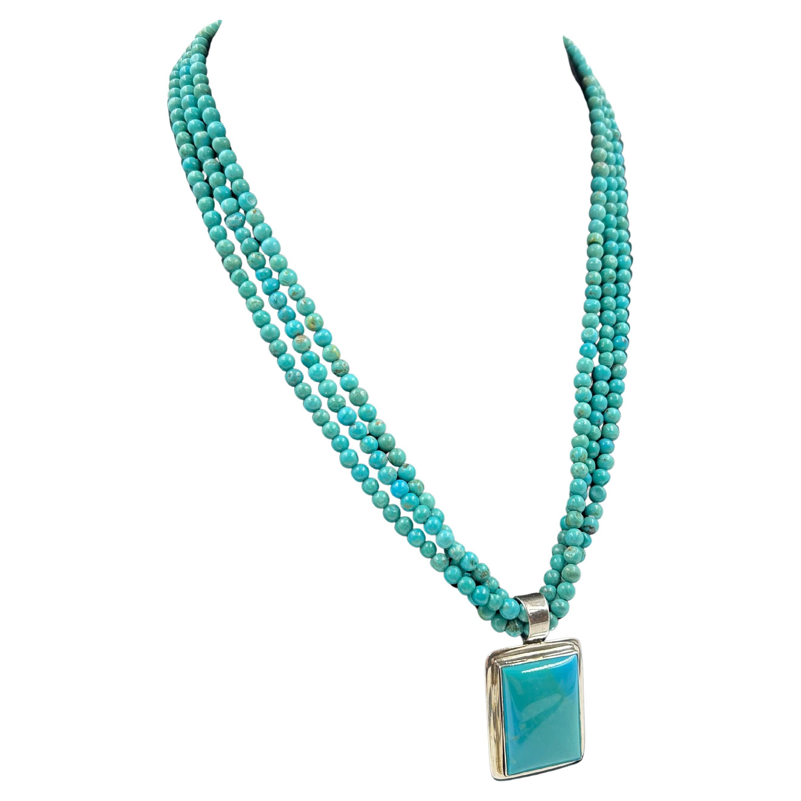Ce collier comporte trois brins de perles turquoise de forme ronde avec une finition non polie, ce qui lui confère un aspect naturel et vibrant. Les perles sont de petit diamètre et sont enfilées de manière à créer un motif en gradins. Le collier se