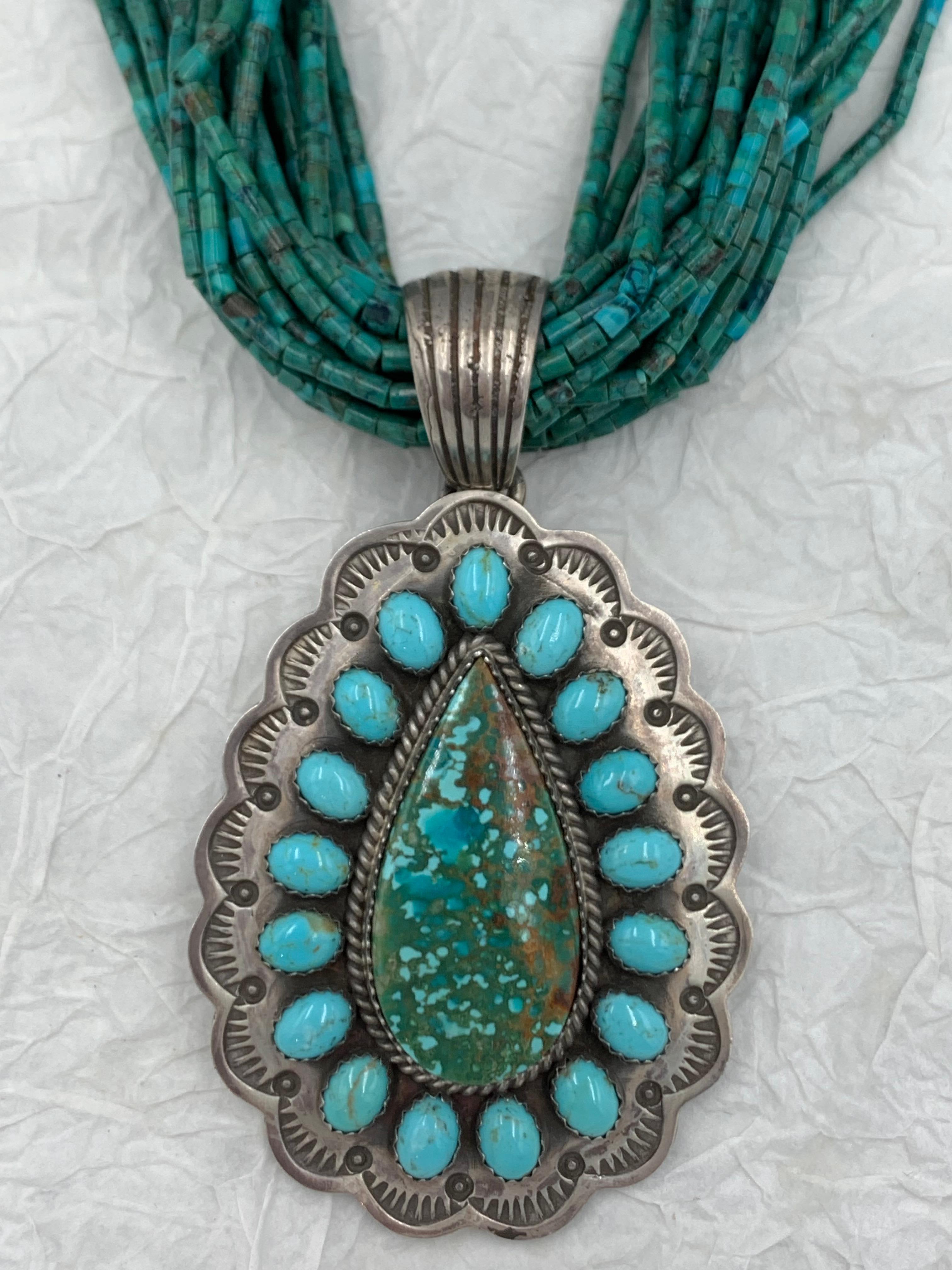 Sterling silver old style pendant by Navajo silversmith Leonard James. A pear-shaped turquoise stone in the center is surrounded by 17 smaller turquoise cabochons. The sterling silver pendant is 1 7/8” x 2 1/2” and signed “L James S/S.”

Twenty two