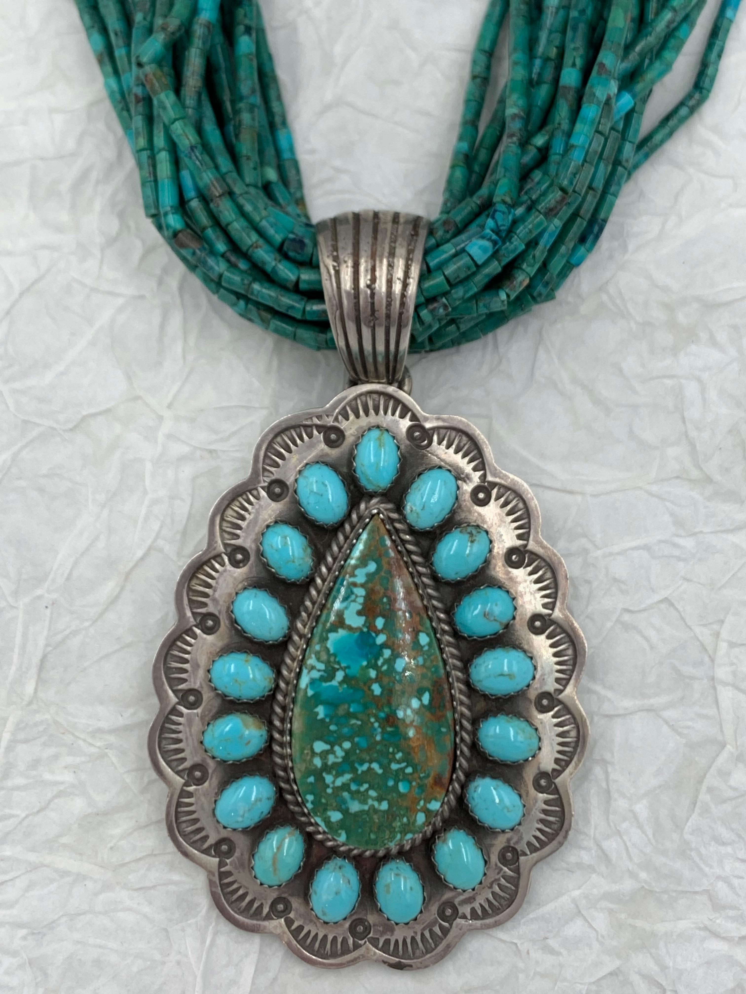 Ciondolo in argento sterling vecchio stile dell'argentiere Navajo James. Una pietra di turchese a forma di pera al centro è circondata da 17 cabochon di turchese più piccoli. Il ciondolo in argento sterling misura 1 7/8