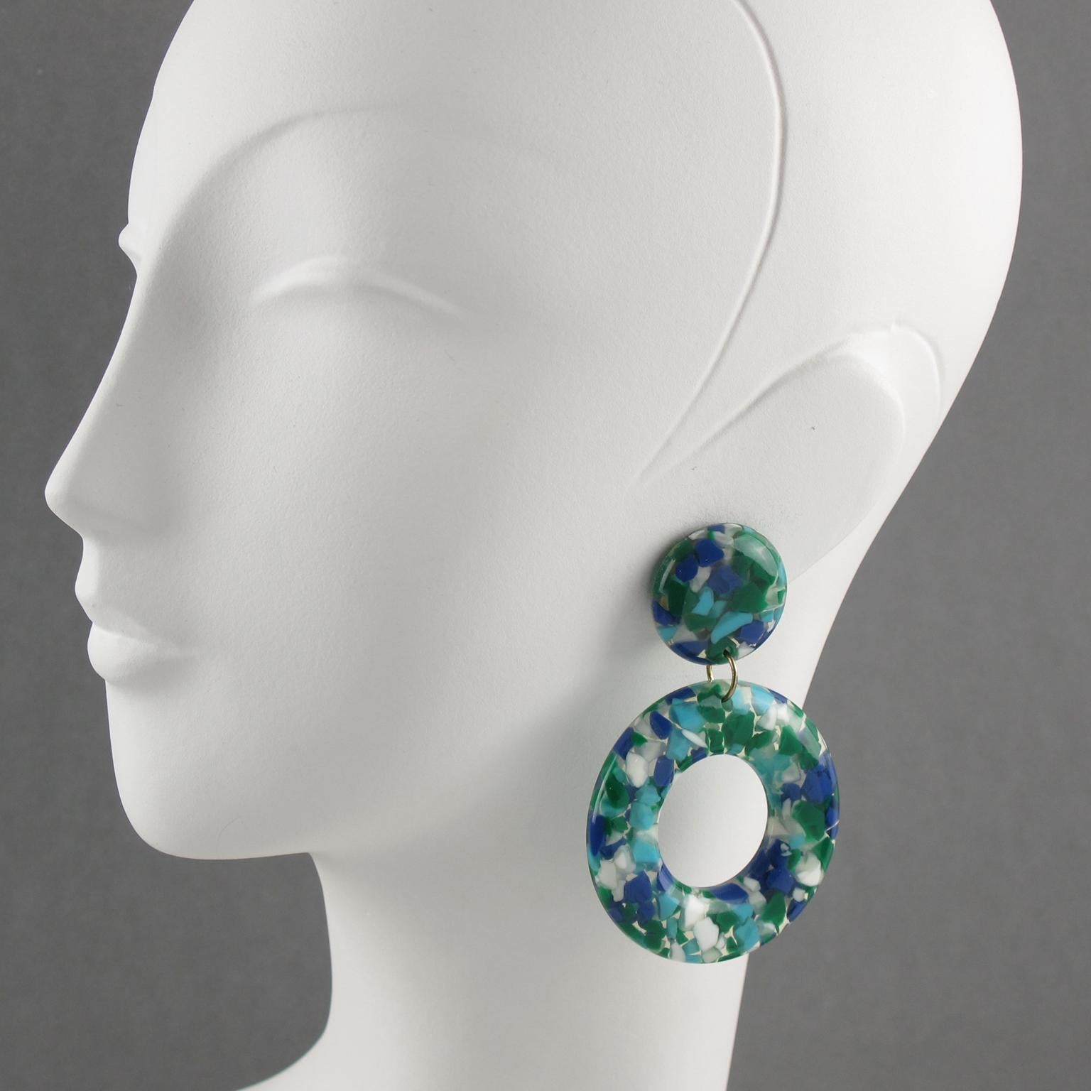 Beautiful bright colors oversized lucite clip-on earrings. Large donut dangling shape with a geometric design featuring clear lucite with colorful tiny chunk inclusions. Assorted colors of cobalt blue, emerald green, white and arctic blue. No