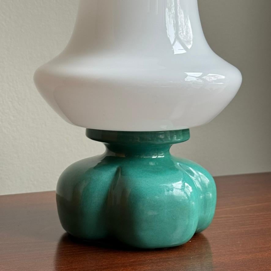 A petite, sculptural table lamp with a terracotta base, glazed in a vivid turquoise, with an opaque, milk-glass shade. 

This table lamp was manufactured by Osvětlovací Sklo during the 1960s and was designed by Czech designer, Ivan Jakeš. This table
