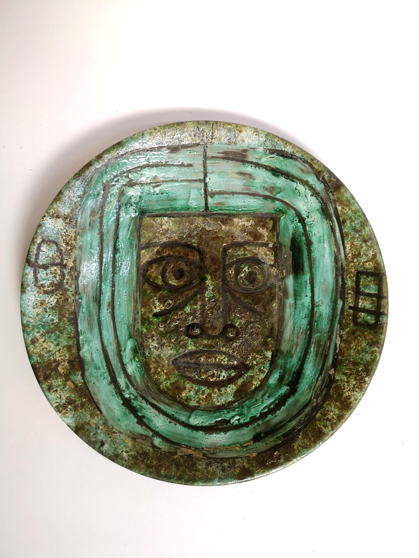 This signed piece by renowned Hungarian ceramist Zsuzsanna Karacsonyi from the 1970’s features a primitive face in folk art style. The simple figurative design dominates the circular ceramic wall plate, a not so ordinary artifact from mid-century