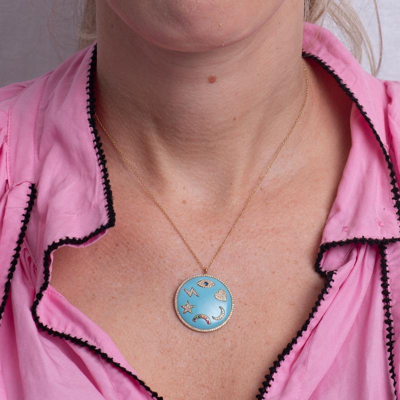 A 14 karat yellow gold and turquoise enamel medallion necklace featuring an evil eye, heart, moon, rainbow, star, and lightning bolt accented in diamonds and gemstones. It is set on an adjustable 18