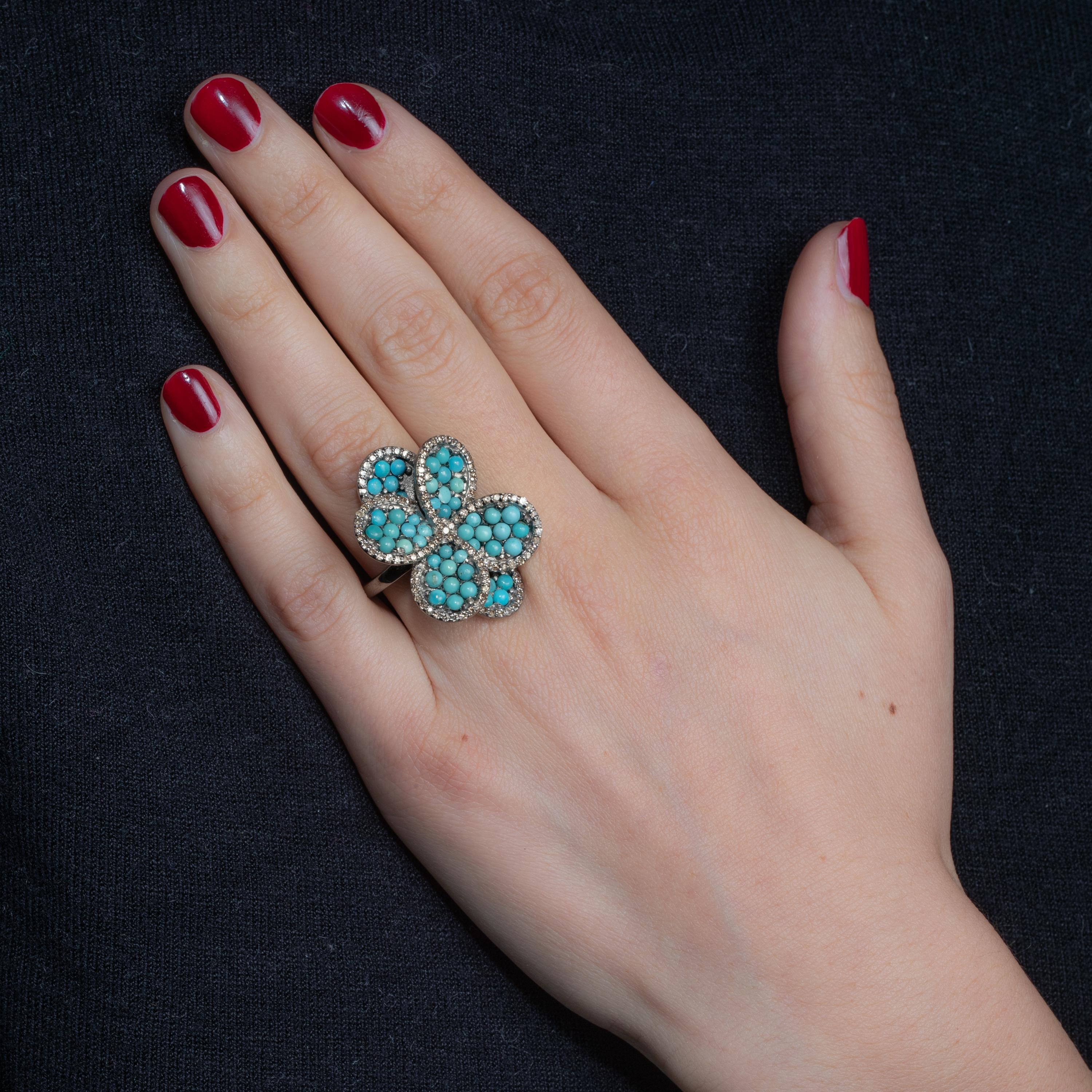 A flower petal ring of round turquoise stones bordered with pave`-set diamonds.  Set in an oxidized sterling silver.  Carat weight of turquoise is 4.47 carats, diamonds total 1.12 carats.  Ring size is 7.