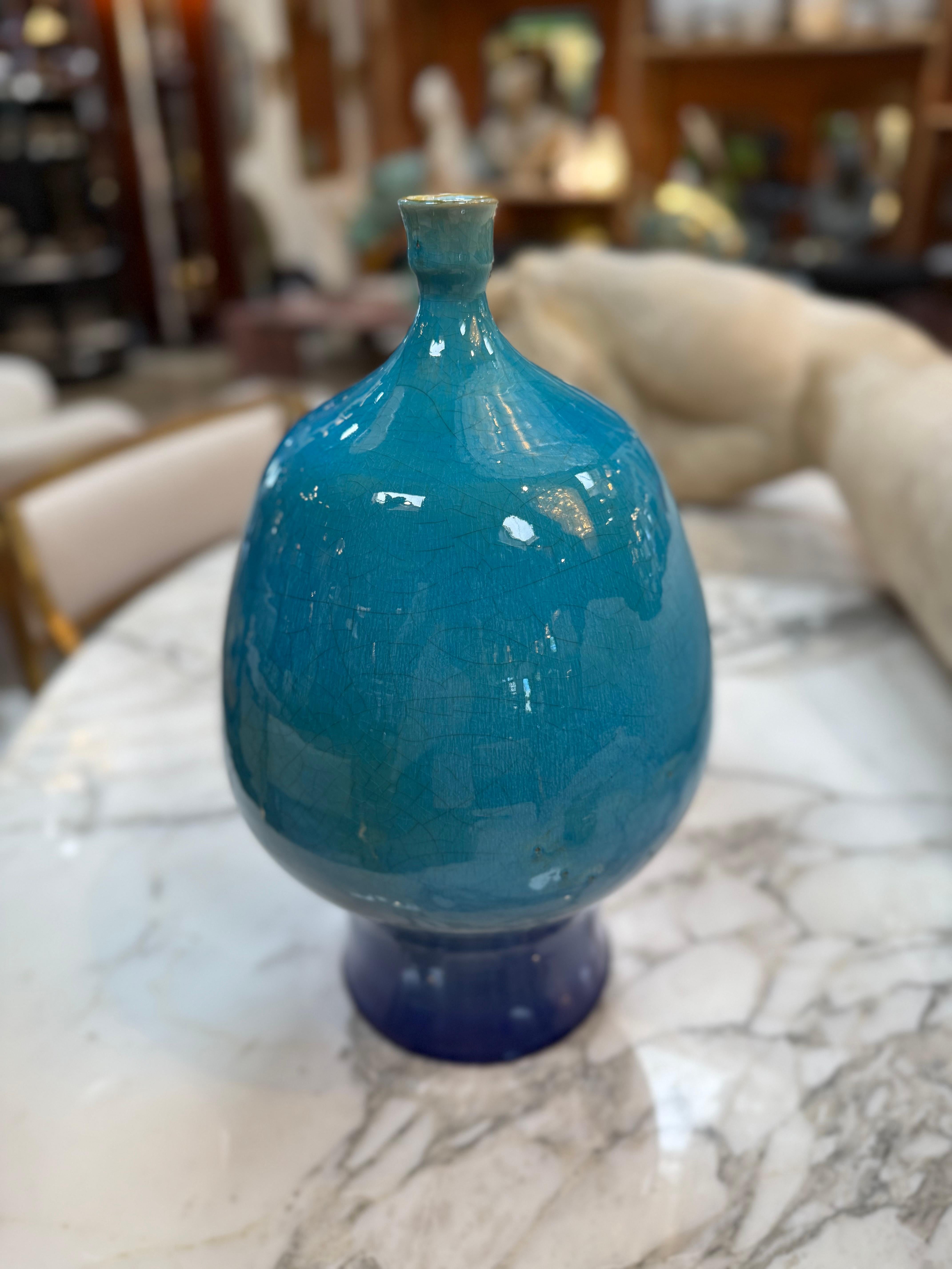 Elegant vase en céramique fabriqué à la main avec un corps arrondi et un col étroit, fini dans une riche glaçure bleu turquoise avec de subtils détails craquelés. La surface brillante et la couleur profonde lui confèrent un attrait à la fois moderne