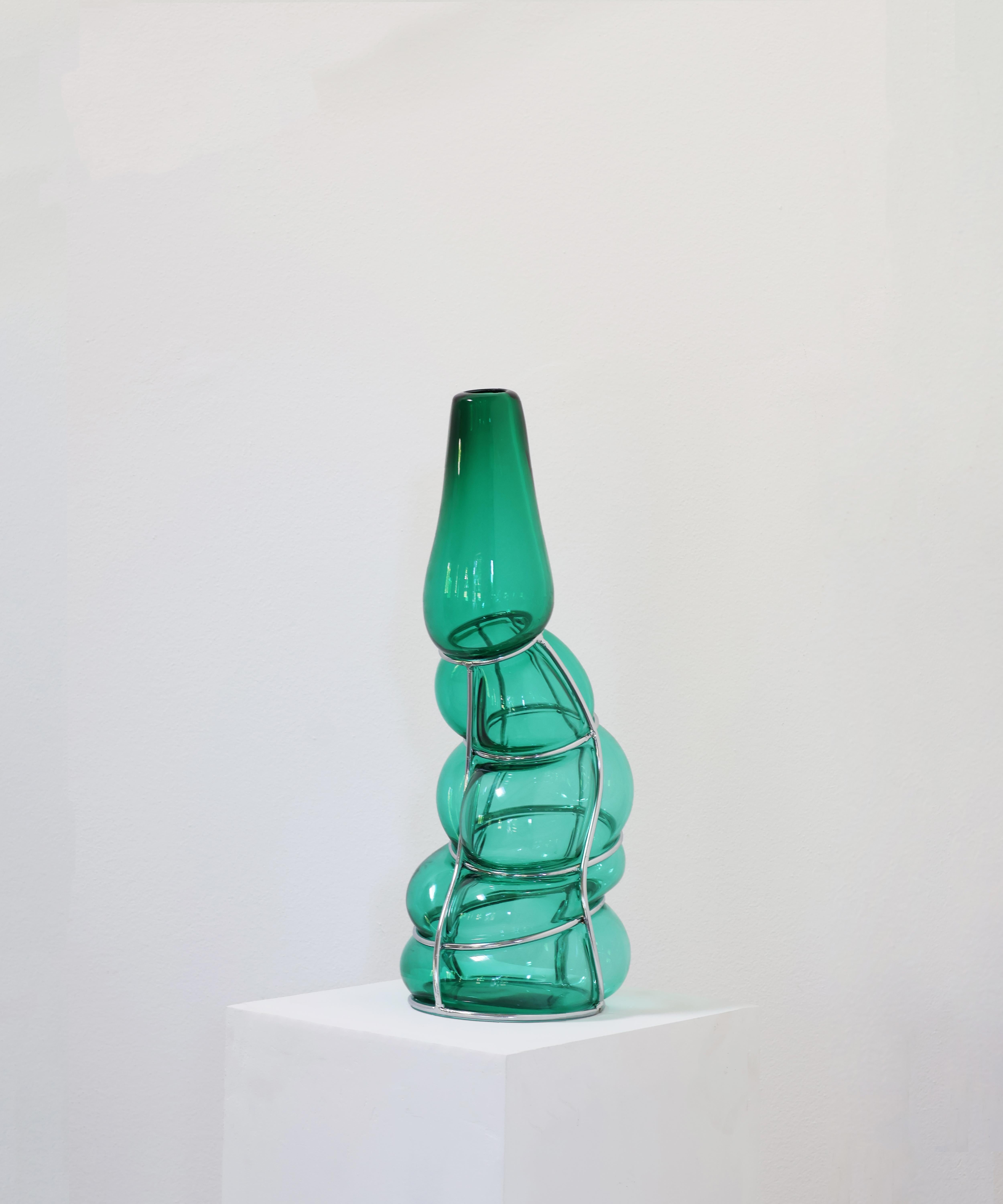 Vaso scultura Babà verde turchese di Alice Crepaldi
Un pezzo unico.
Dimensioni: Ø 24 x H. 52 cm.
Materiali: Vetro di Murano e metallo.

Adornato da uno stelo leggermente più corto ma elegante, questo vaso ingabbiato utilizza la tecnica dello