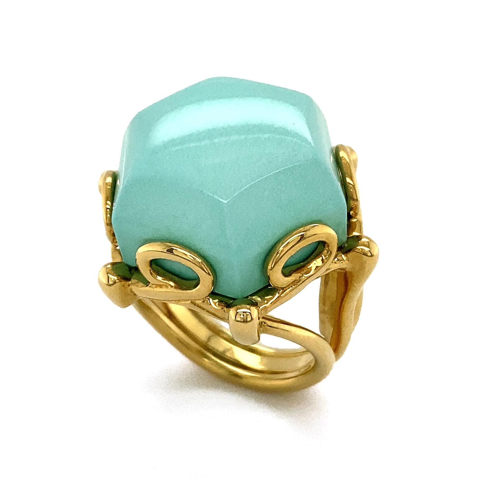 The serene cyan shade of turquoise is showcased in this ring. The gem is cut into a hexagon shaped cut, allowing the light to highlight its singular tone. 18k yellow gold forms the band as well as glides into a pattern of loops for a decorative