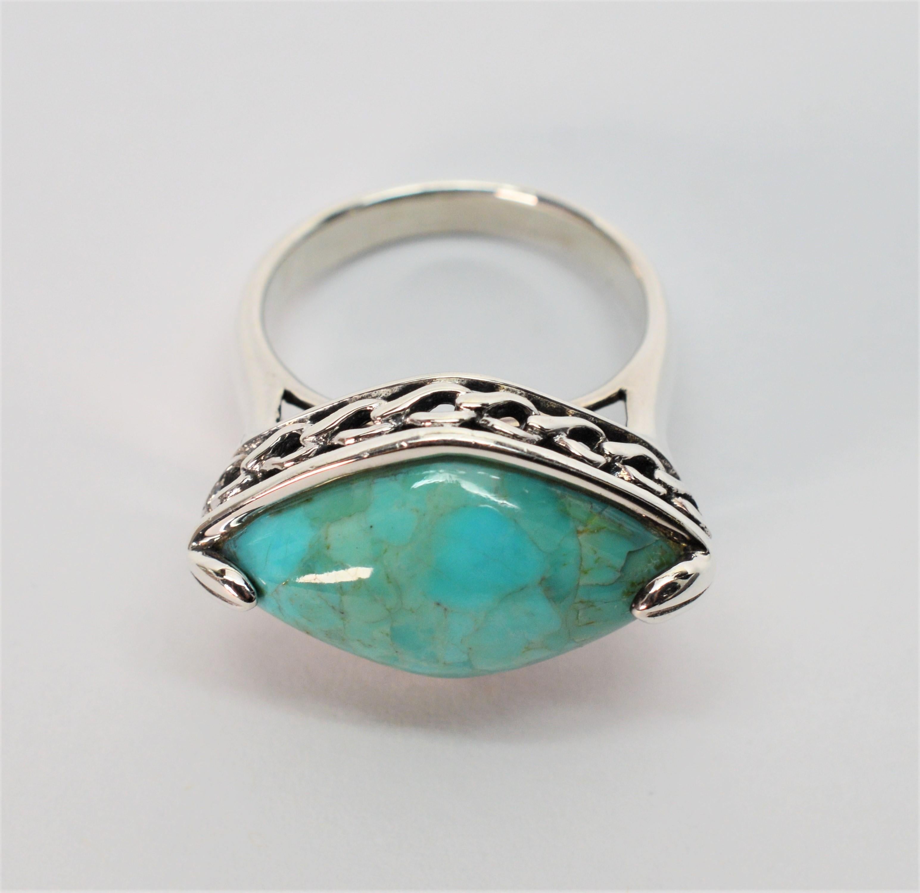In an unusual horizontally designed ring setting, this large strong blue-green naturally marbled marquise cut 14 x 23mm polished turquoise cabochon certainly attracts attention. Made in sterling silver, a raised gallery prominently displays this