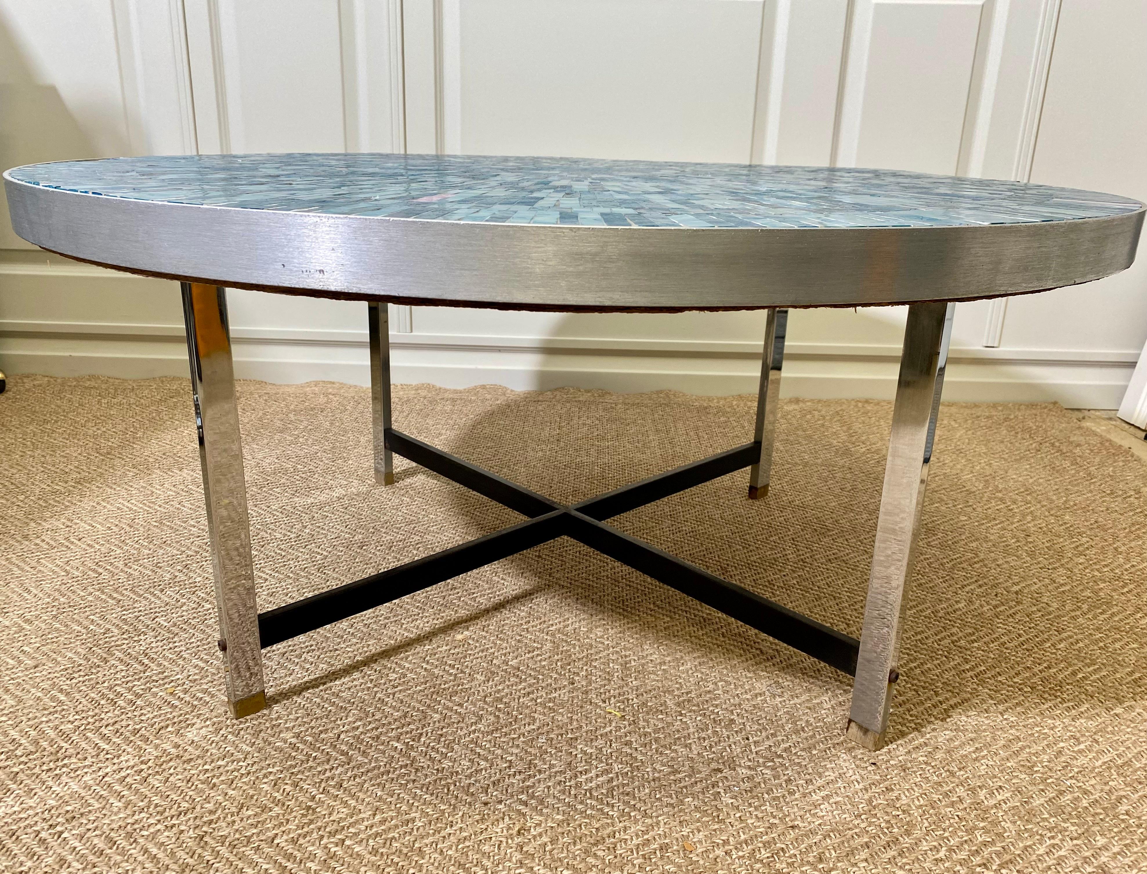 This hand-crafted round mosaic table was created in the Mosaik-Werkstatt (mosaic workshop) of the highly acclaimed German sculptor and mosaicist Berthold Müller-Oerlinghausen in the 1960s.

Framed in a brushed metal band and standing on four wooden